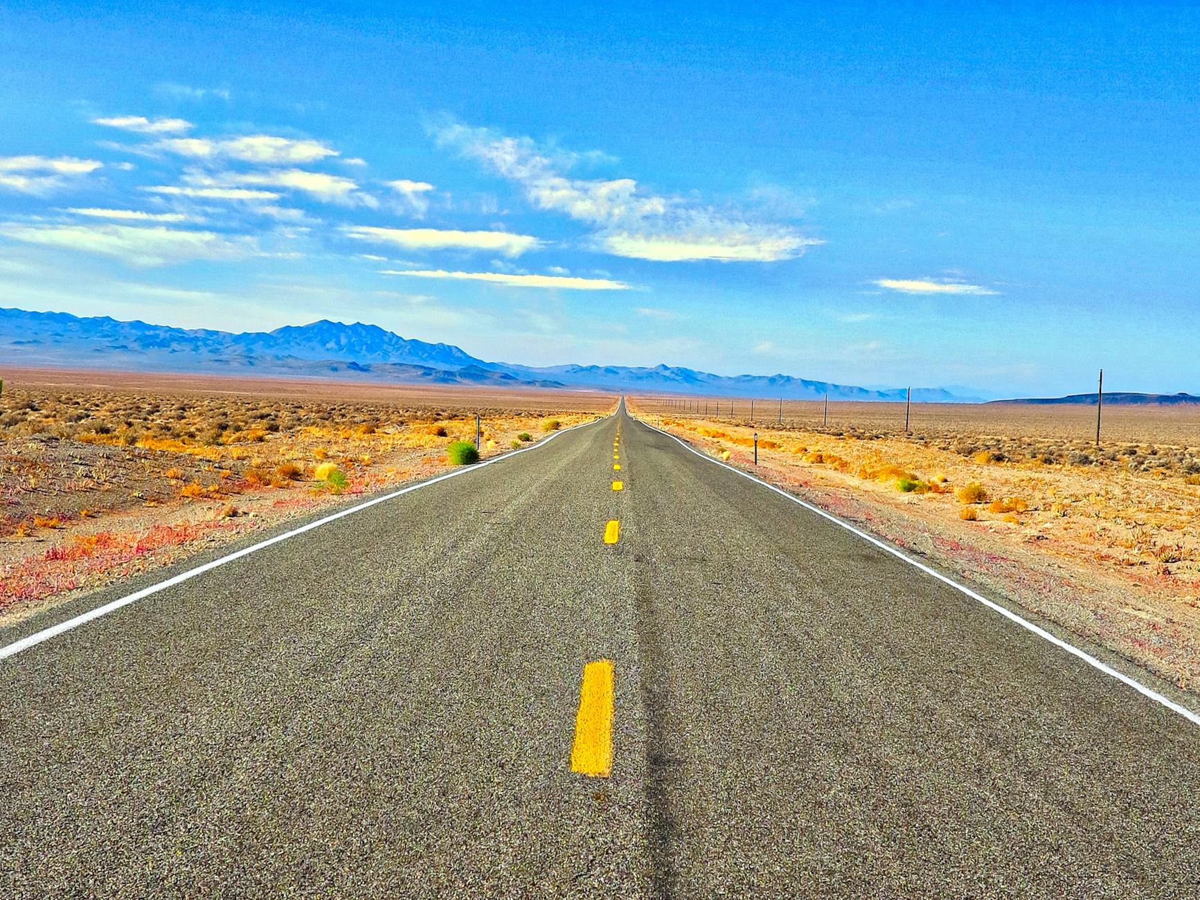 A long straight road in the Nevada desert under a blue sky, perfect for travel and adventure.