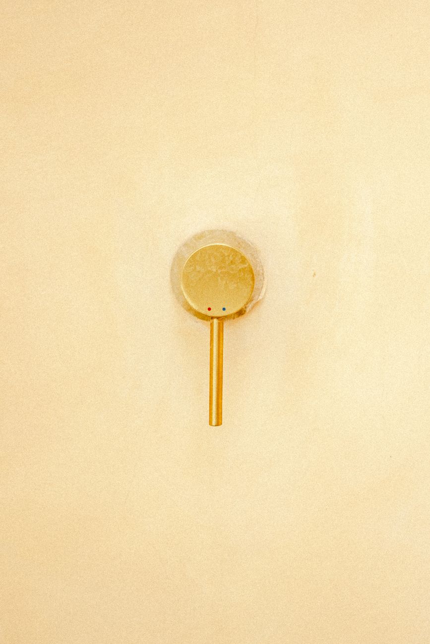A sleek gold water faucet set against a smooth beige wall, exuding simplicity and elegance.
