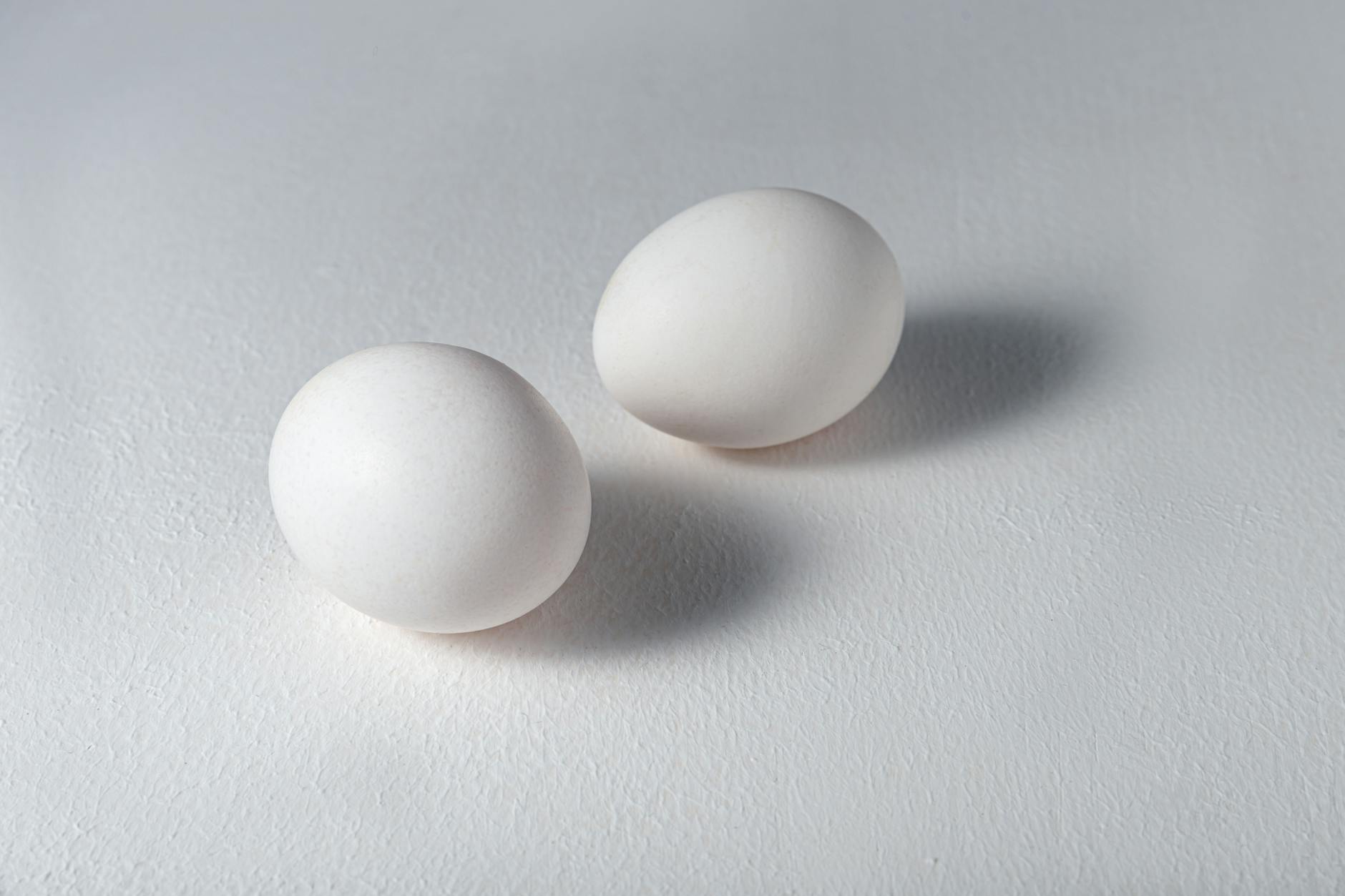 A minimalist image capturing two white eggs with shadows on a white background. Ideal for food and lifestyle themes.