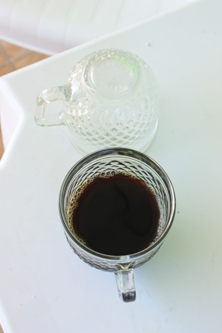 A clear glass cup filled with dark liquid beside an empty glass on a white surface.