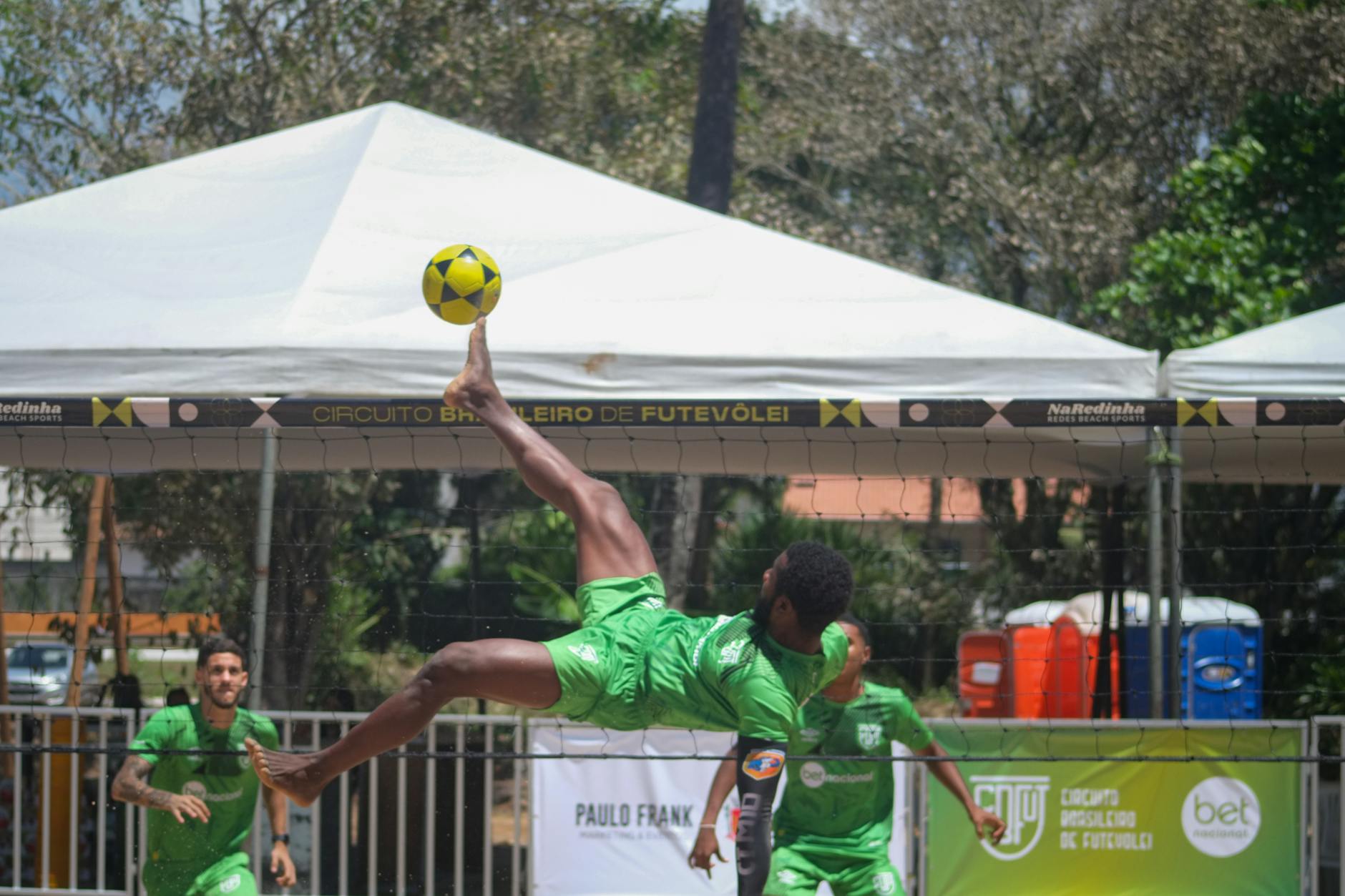 Athletes showcasing futevôlei skills at a sunny tournament in Ilhéus, BA, Brazil.