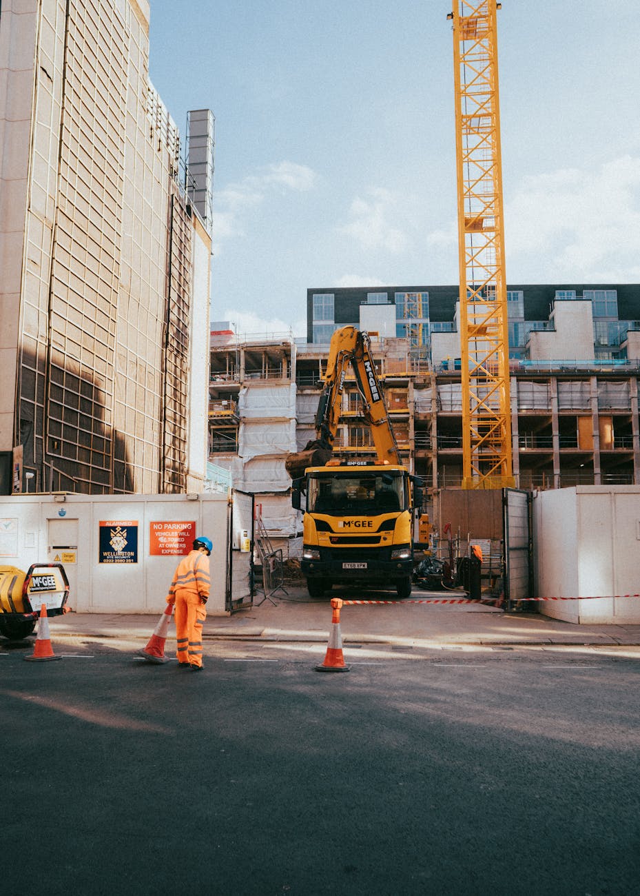 City construction site featuring worker, machinery, and urban surroundings in progress under bright daylight.
