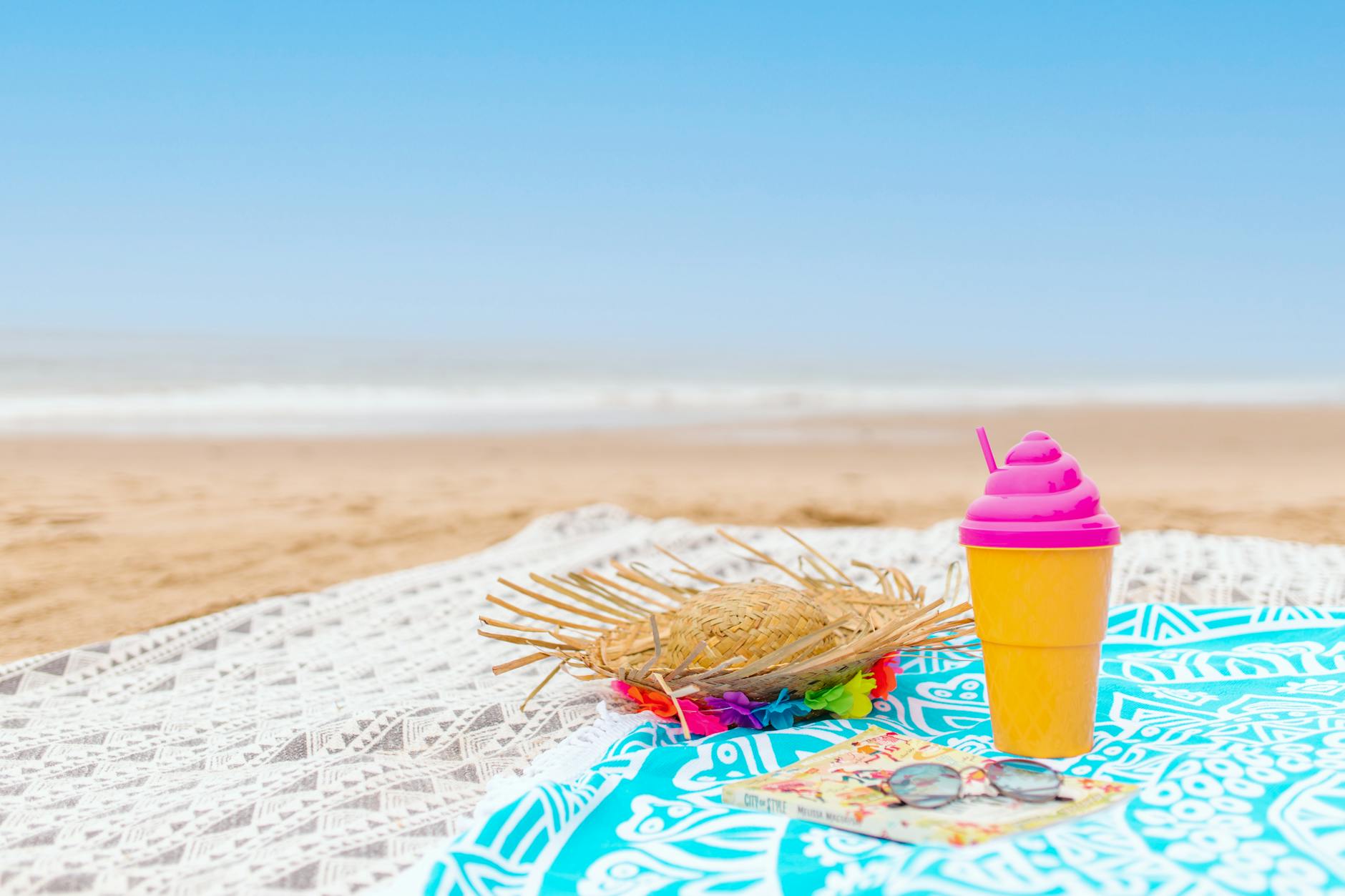 Refreshing summer scene on a sandy beach with a colorful drink, woven hat, and vibrant cloth.