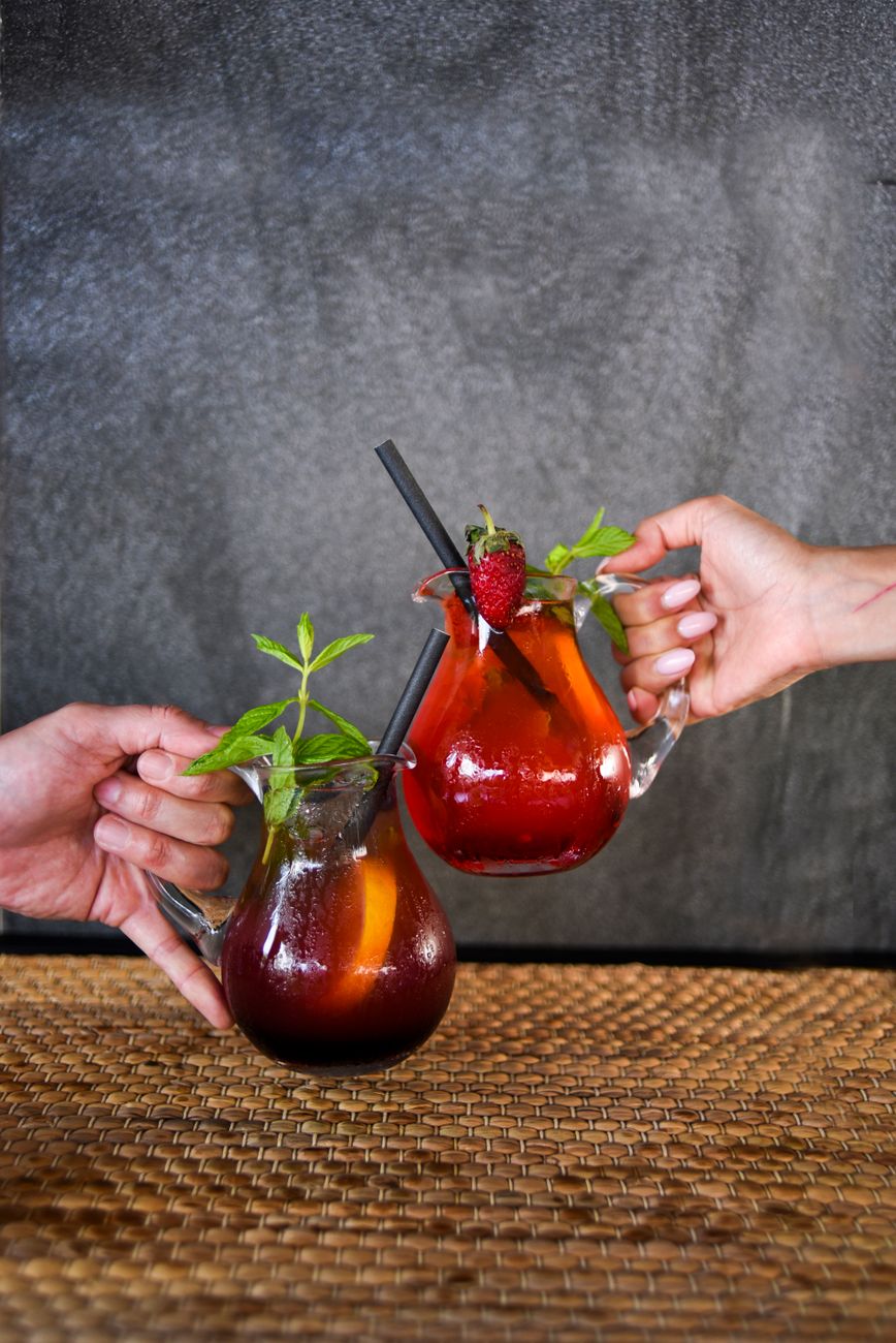 Vibrant summer cocktails in glass mugs, garnished with fruit and mint, held in a celebratory toast.
