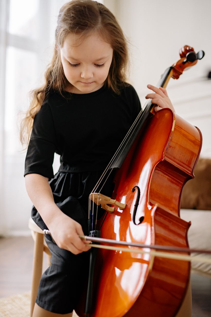 Young girl practicing the cello indoors, focused on learning music.