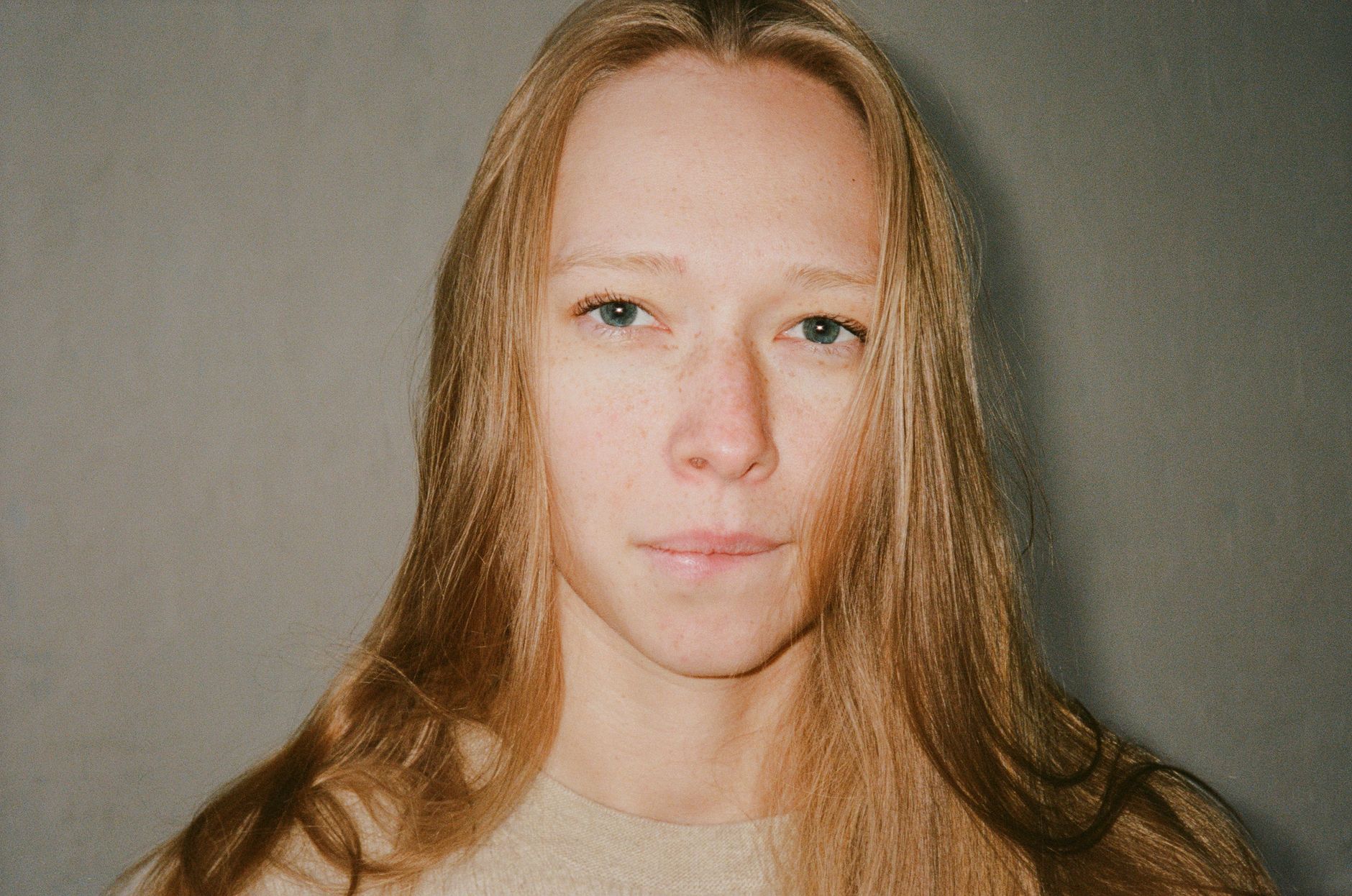 A serene close-up portrait of a woman with blond hair and freckles indoors.