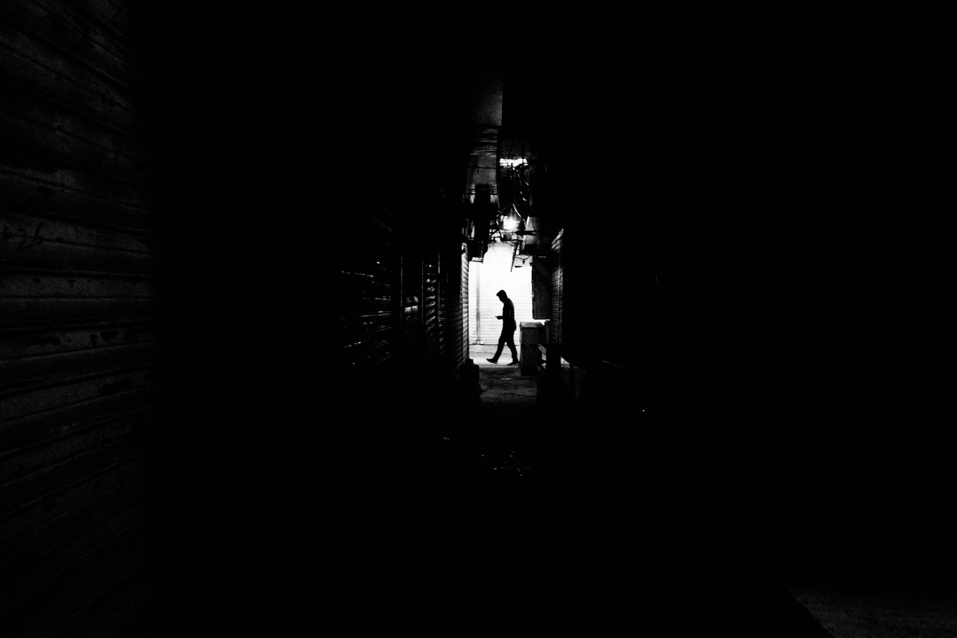 Black and white photo capturing a silhouette of a man walking in a dimly lit alley.