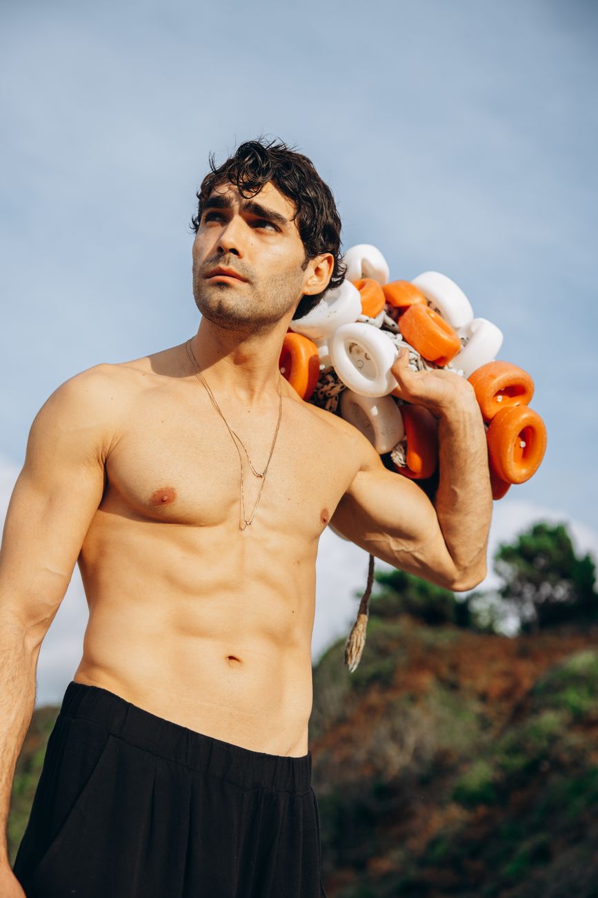 A fit man stands outdoors holding a bundle of lifebuoys, showcasing strength.
