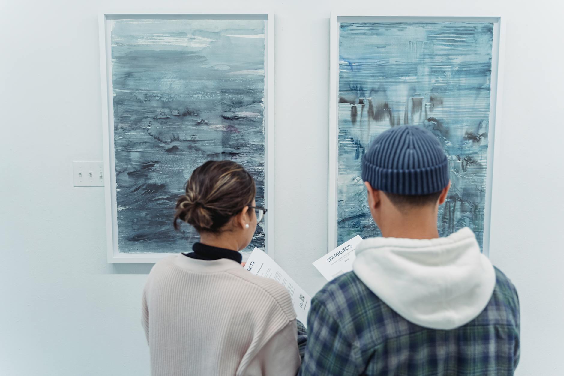 Two people observe modern abstract paintings at an art gallery exhibit.