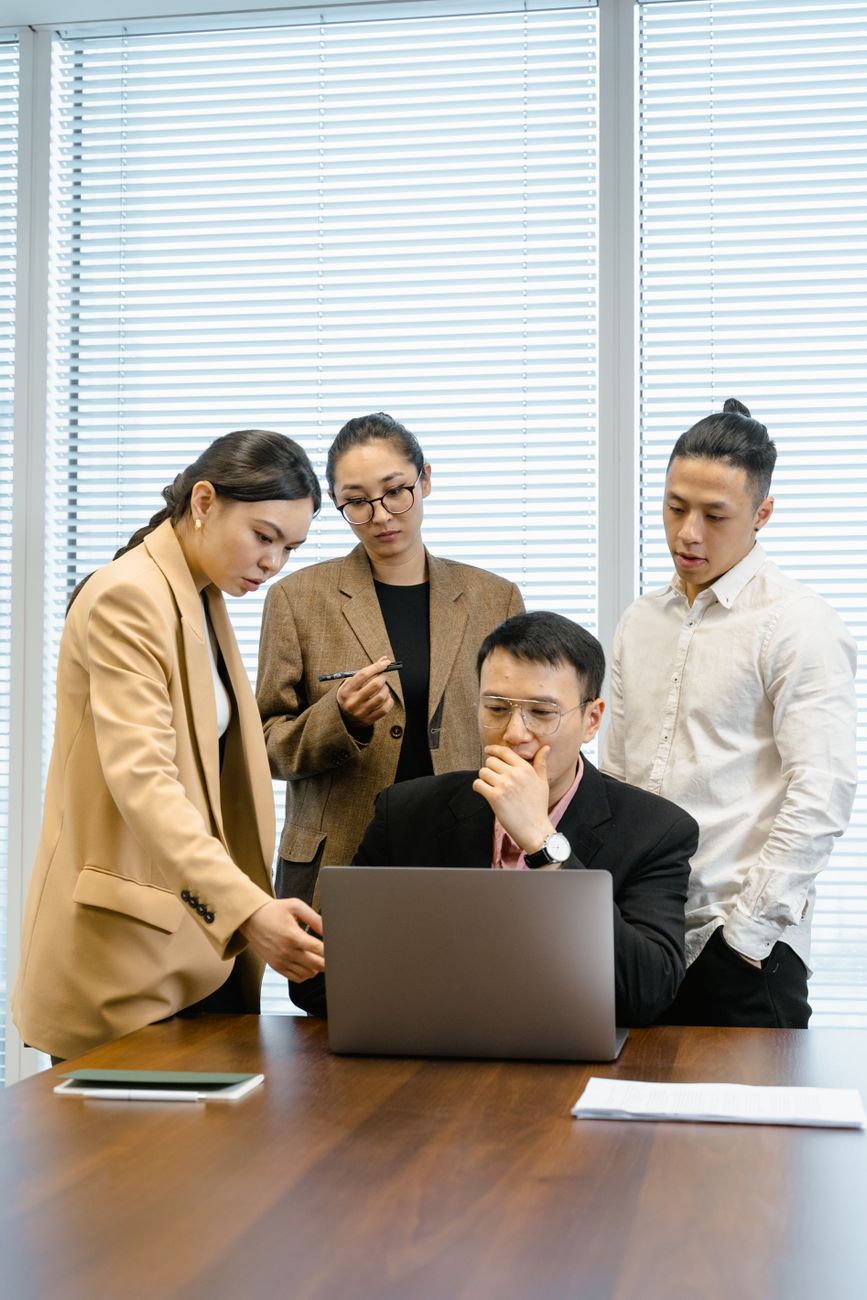 A group of colleagues engaged in a meeting, discussing around a laptop in a modern office.