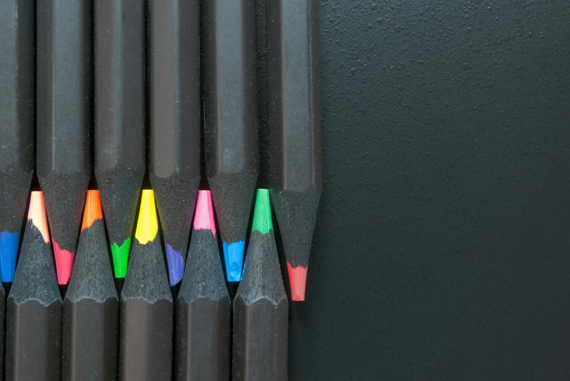 A close-up view of vibrant colored pencils aligned on a textured black surface.