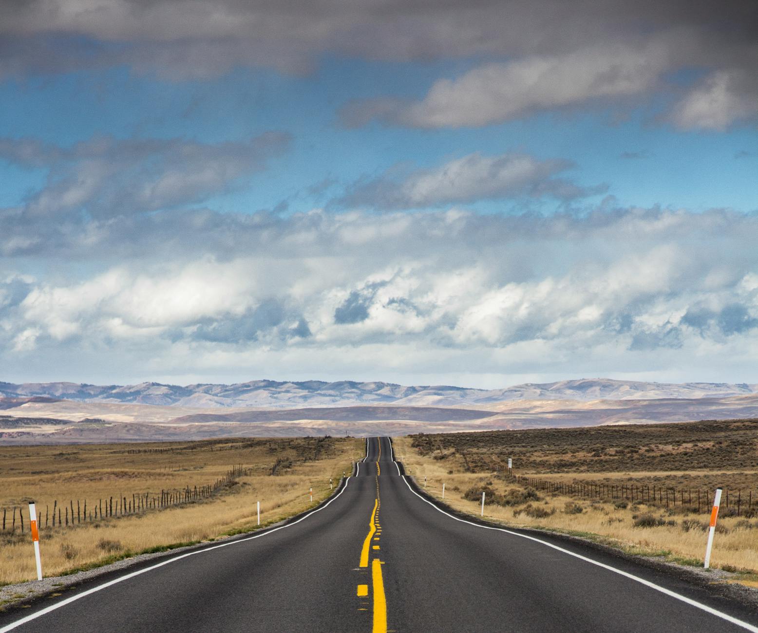 Dramatic view of a long, open road through a vast desert landscape under cloudy skies.