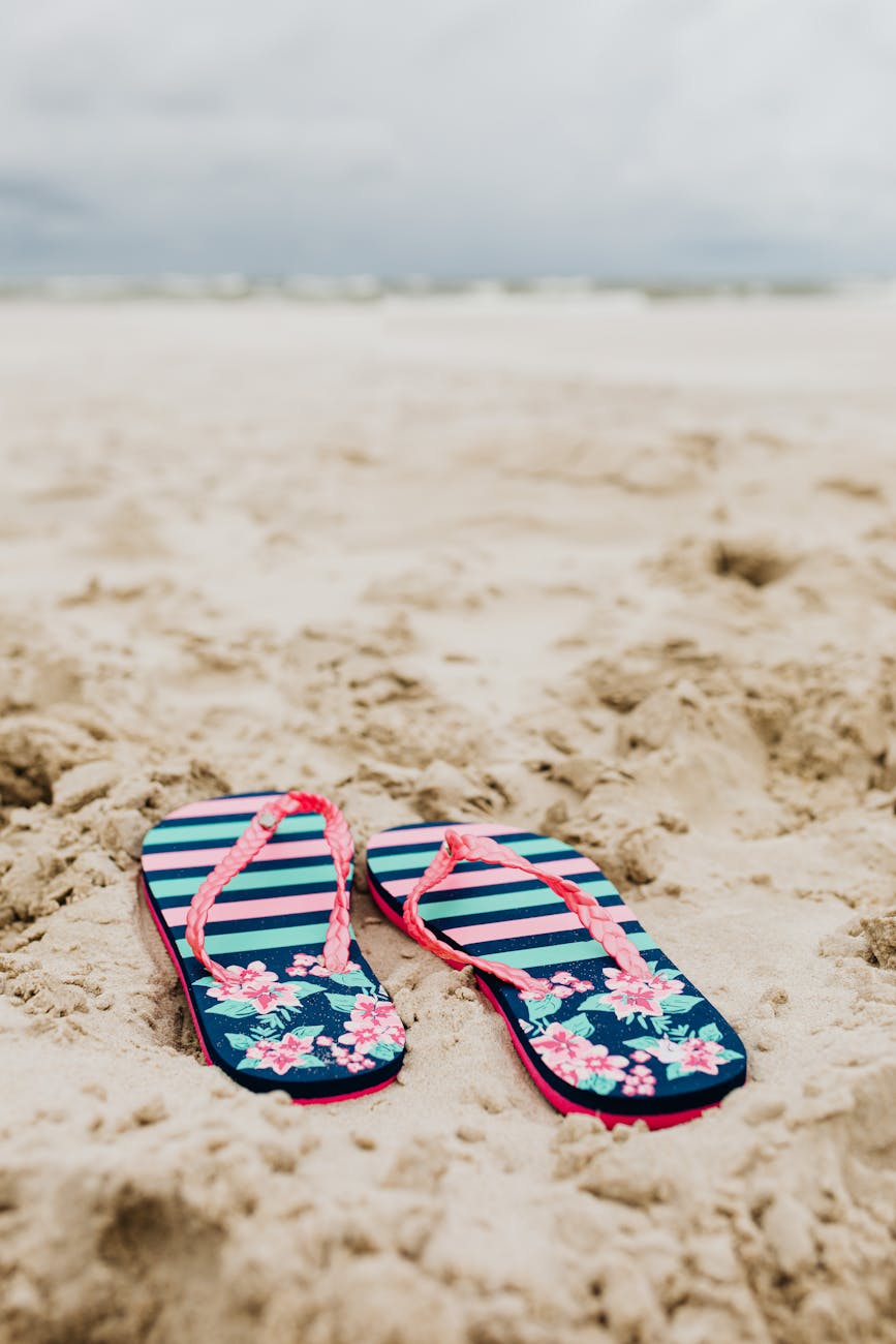 Vibrant flip flops resting on sandy beach, evoking a tropical summer vibe.
