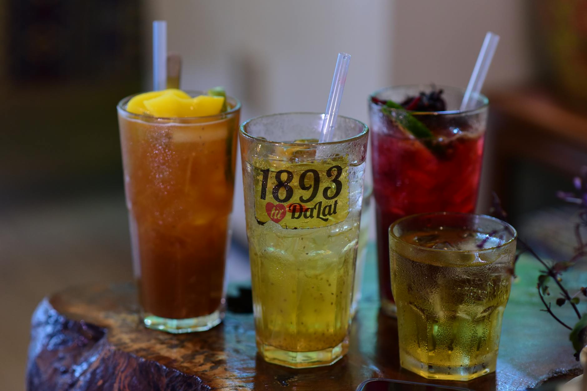 A variety of colorful iced drinks served in glasses with straws on a rustic table indoors.