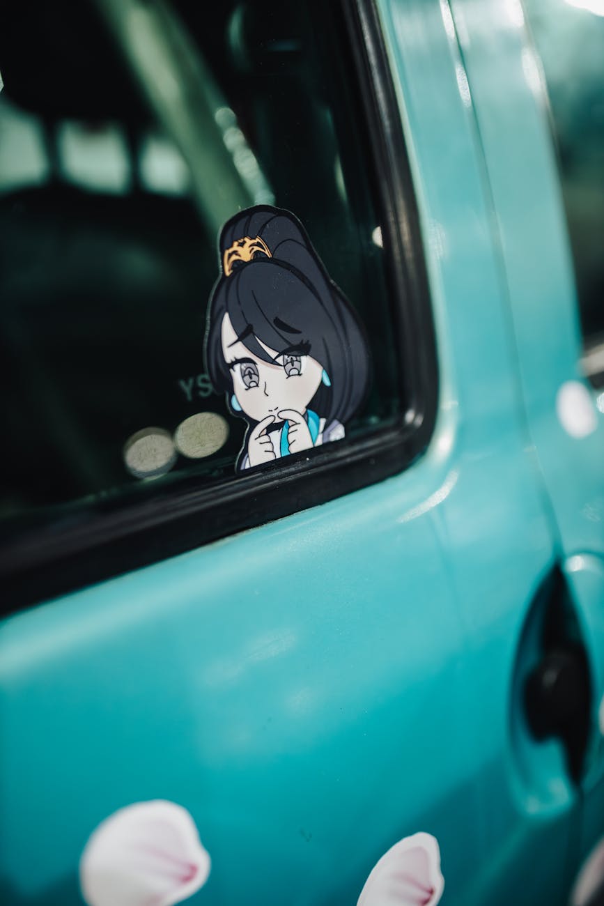 Close-up of an anime character sticker on a blue car window, showcasing vibrant artwork.