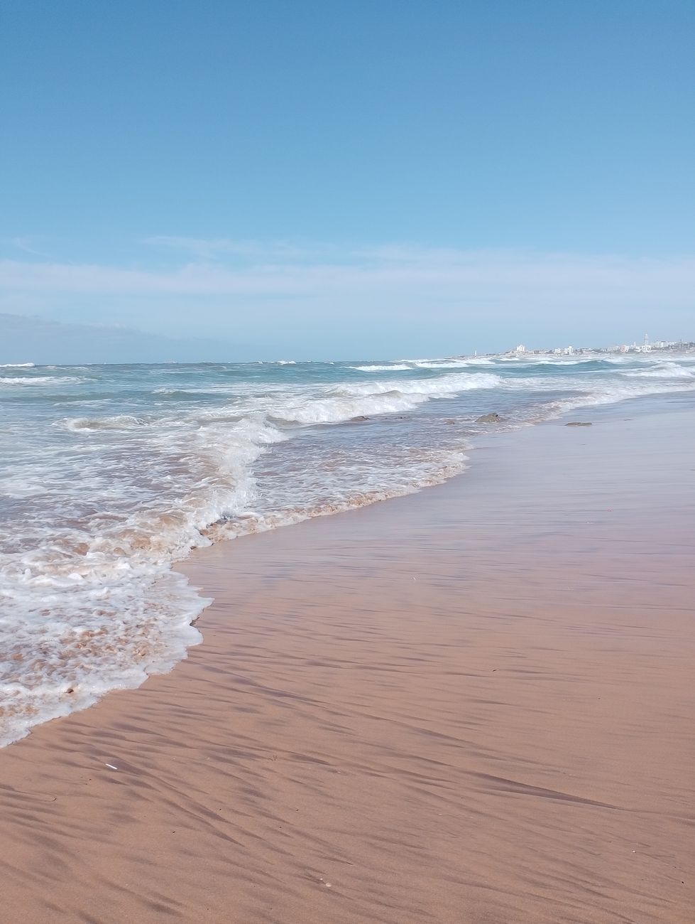 A tranquil beach with gentle waves under a clear blue sky in Casablanca, Morocco.