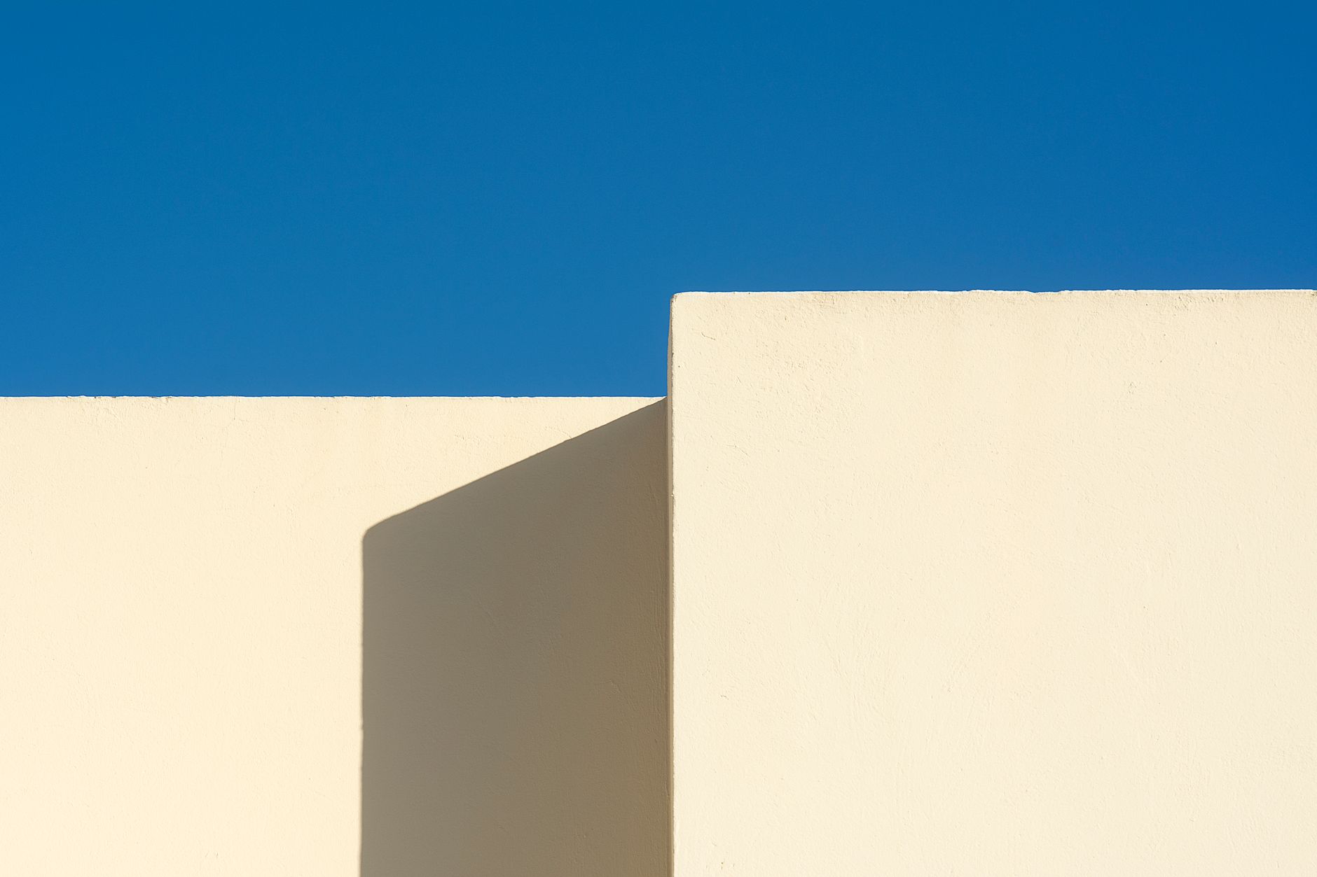 A minimalist architectural structure with white walls contrasting a vivid blue sky.