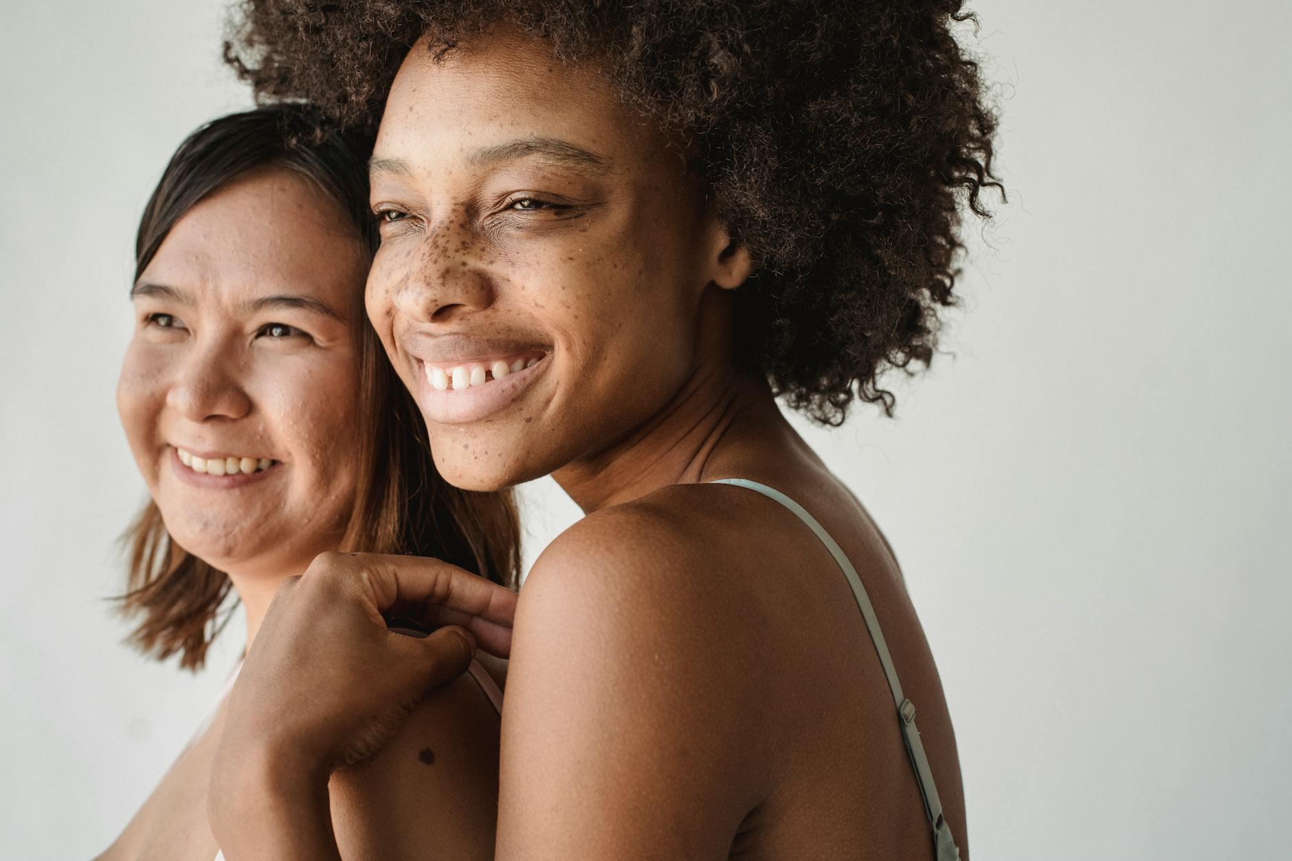 Two diverse women smiling confidently, showcasing friendship and diversity, on a white background.
