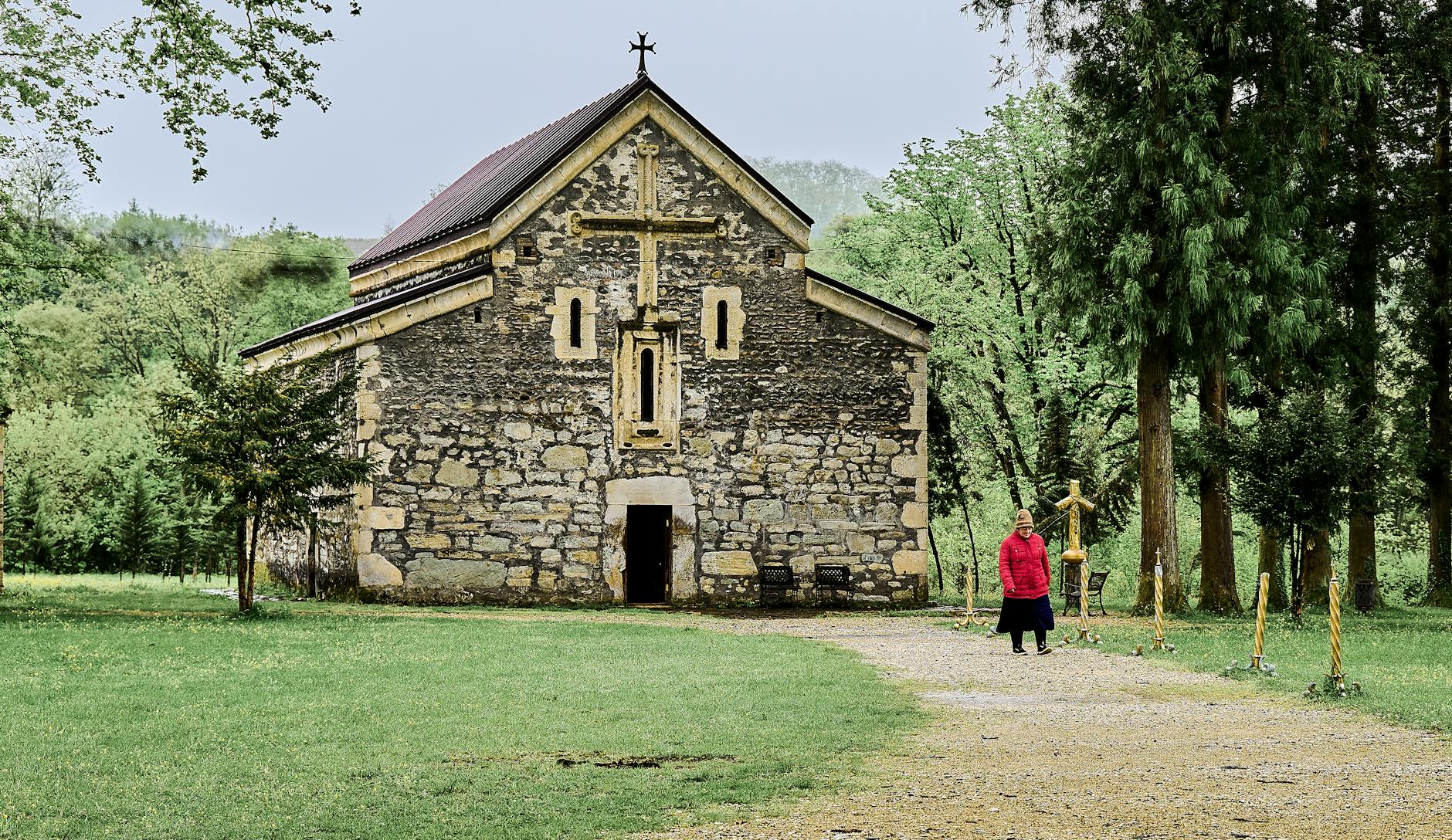 Charming stone church in lush green surroundings with a visitor in Borjomi, Georgia.