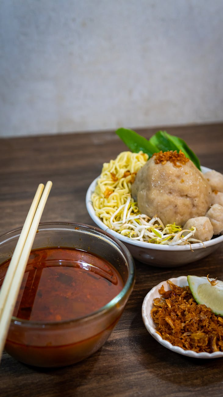 Delicious traditional Indonesian Bakso meatball soup with noodles and spices, served on a wooden table.