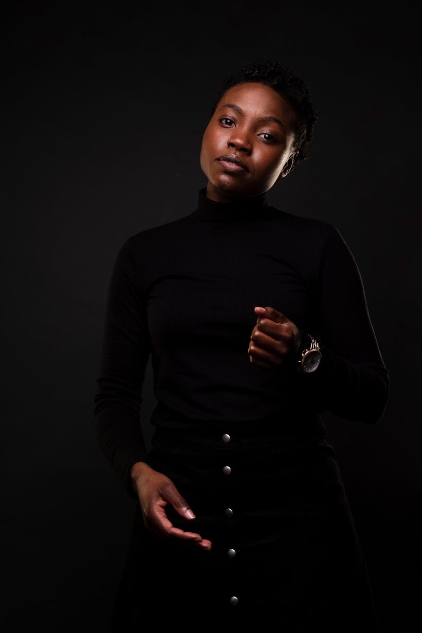 Stylish black woman posing confidently against a dark background in a fashion photoshoot.