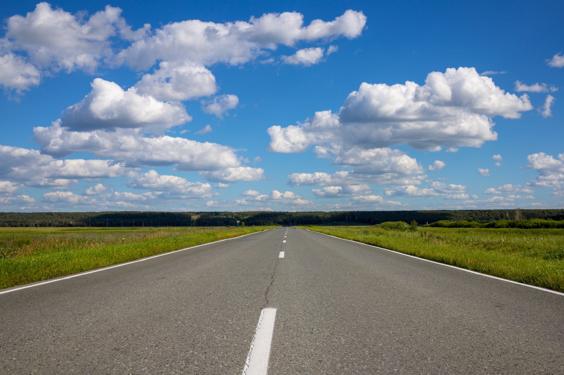 Open countryside road stretching into distance under bright blue sky with fluffy clouds
