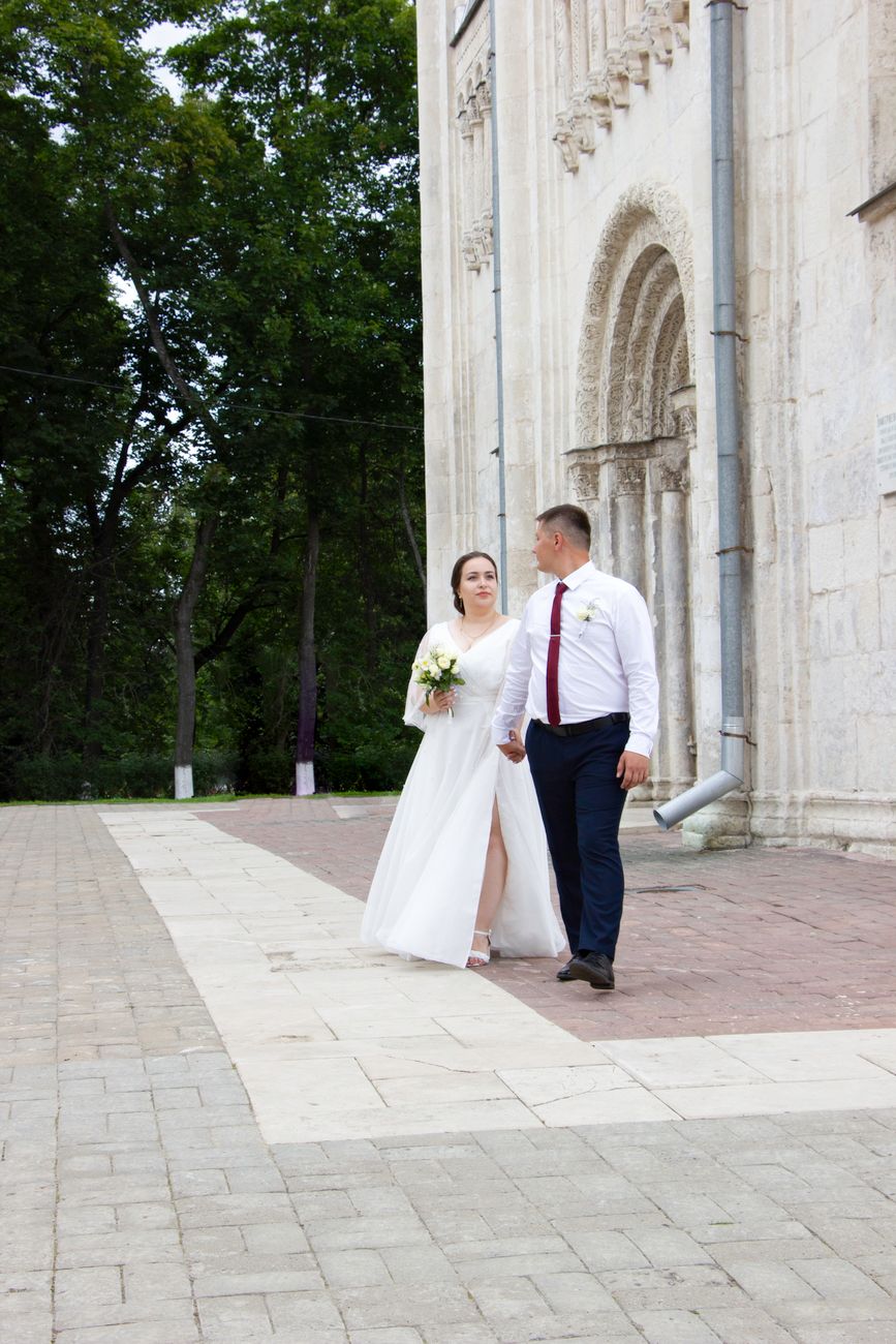 Bride and groom walking outside a historic church holding hands, symbolizing love and unity.