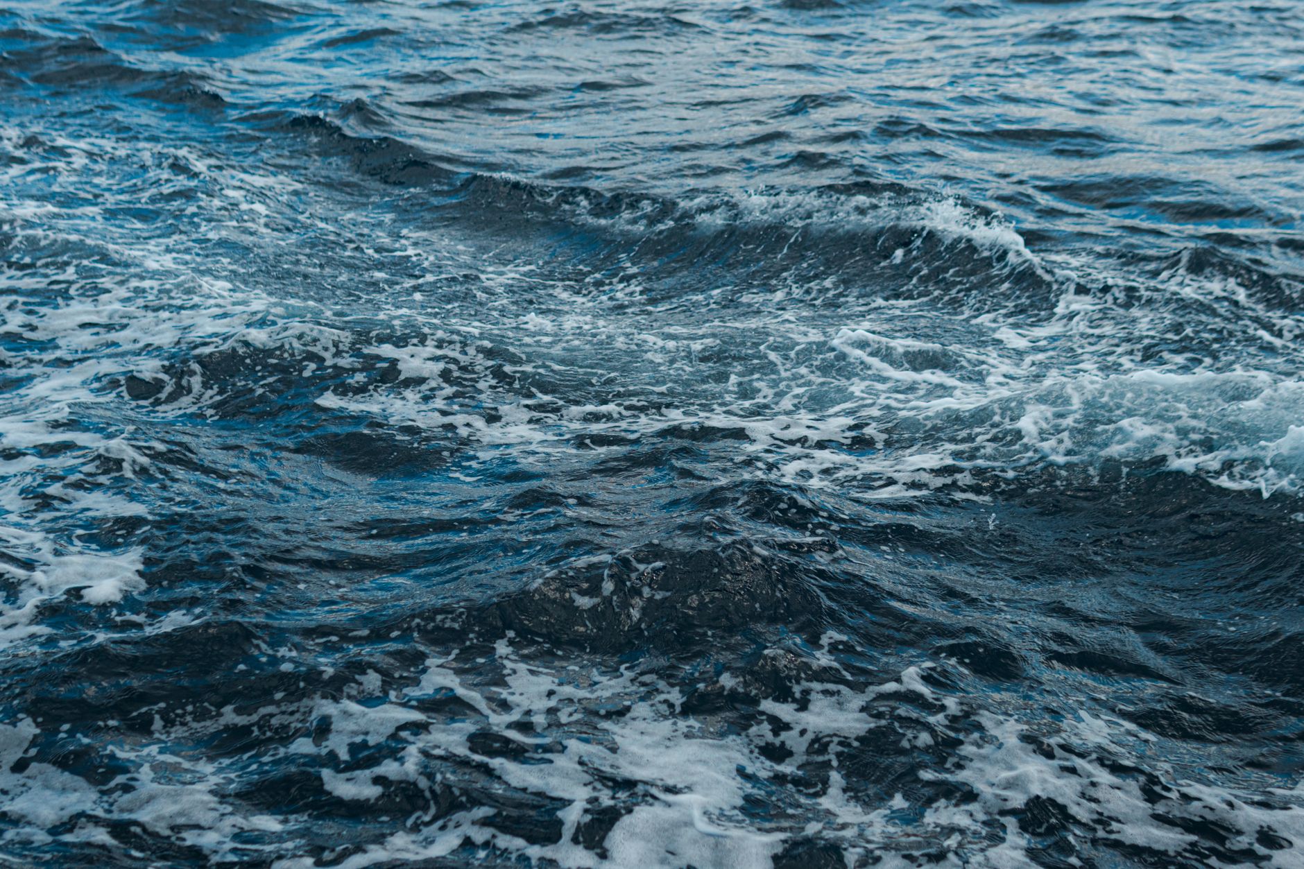Close-up shot of swirling ocean waves and white foam, showing natural movement.