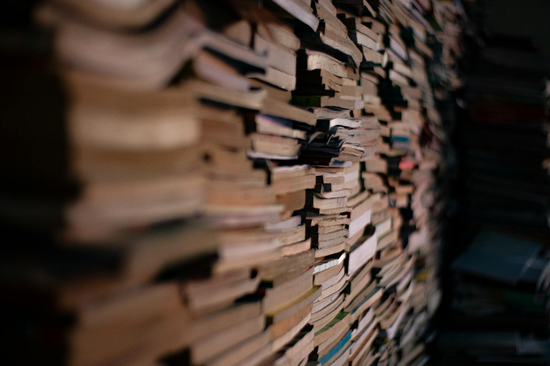A dense stack of books creating a sense of depth and knowledge in a dimly lit room.