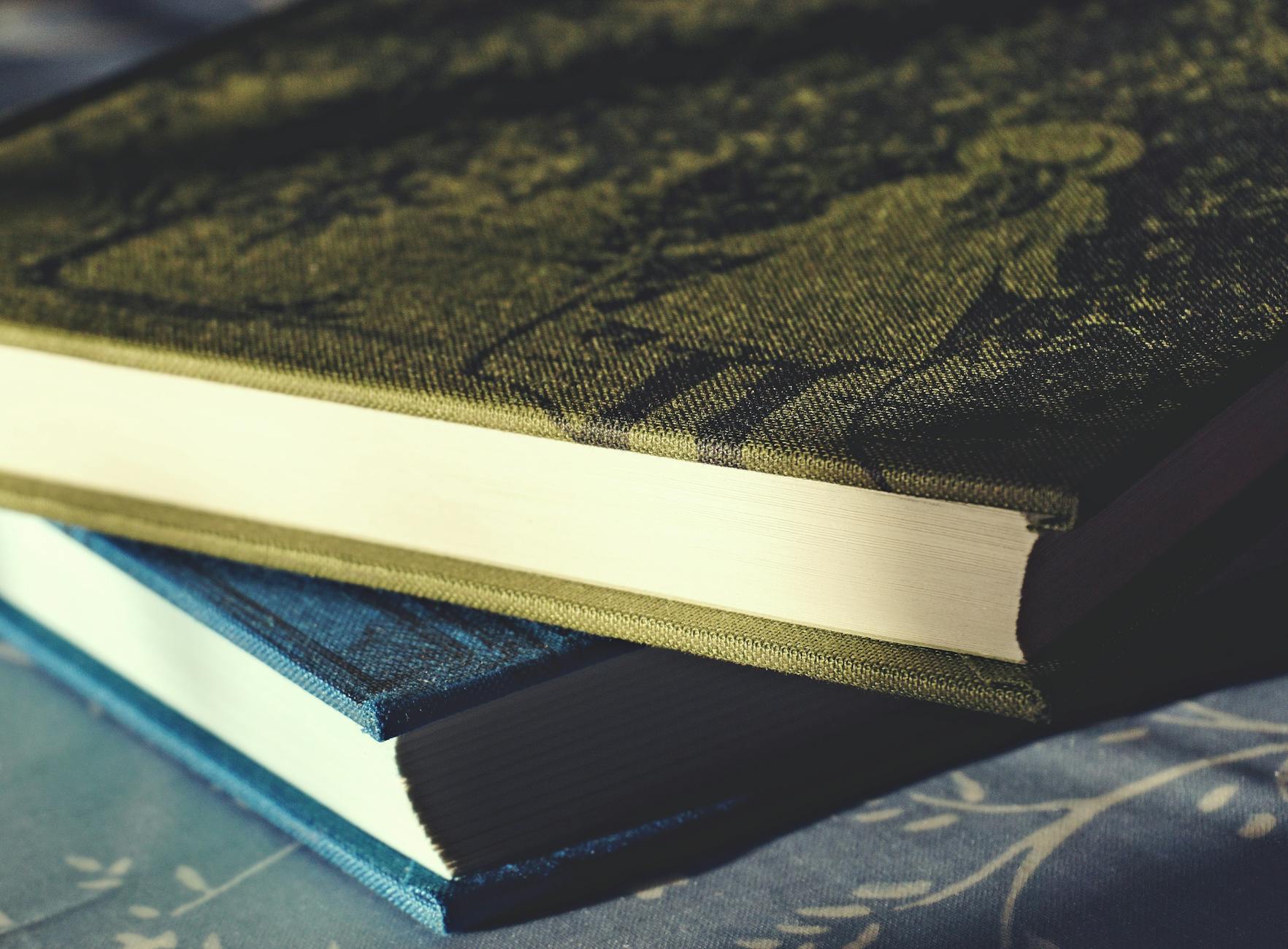 Close-up view of two hardcover books stacked on a patterned surface, capturing intricate cover details.