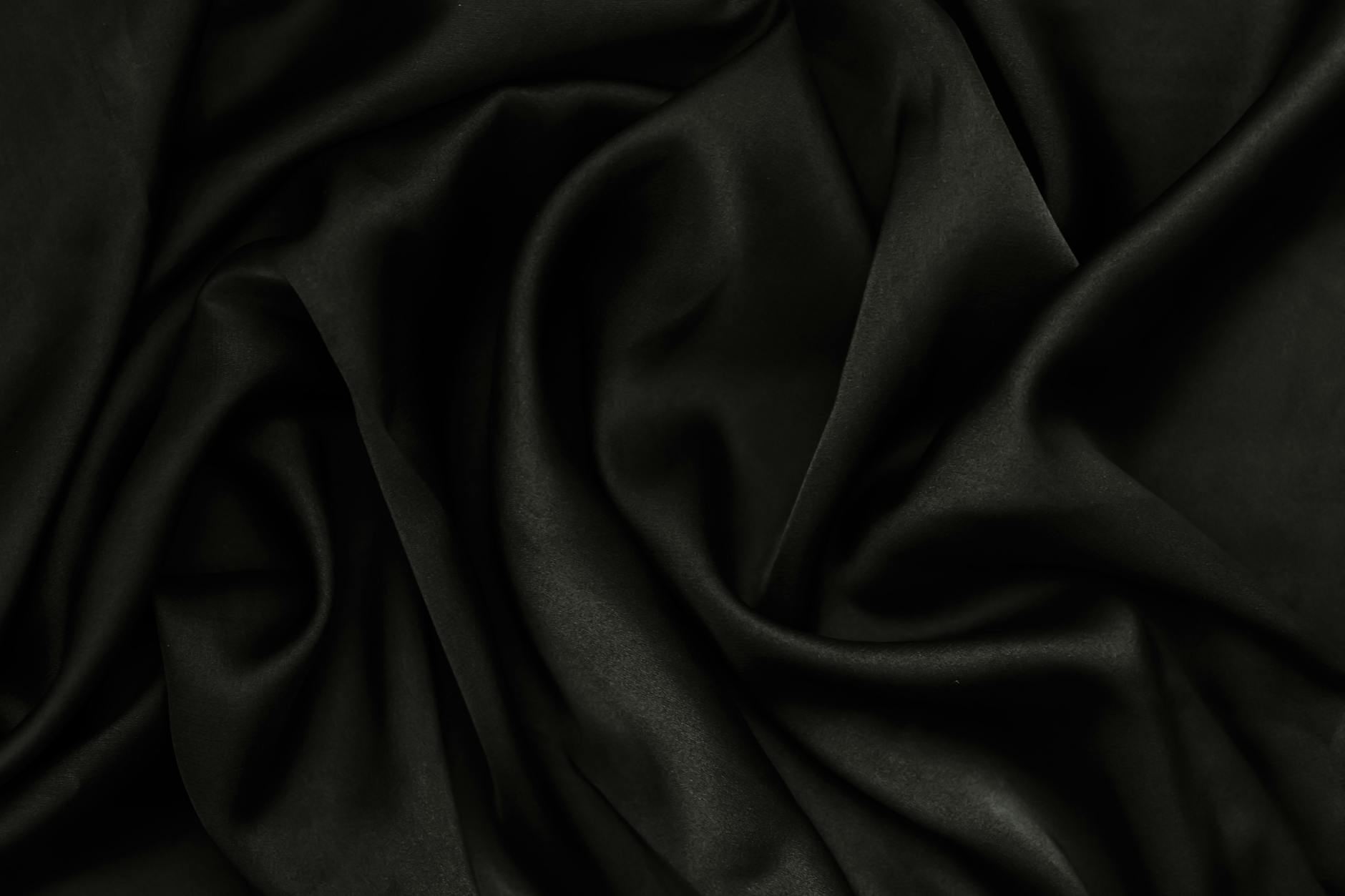 A close-up of smooth black fabric with rippling texture, perfect for background use.