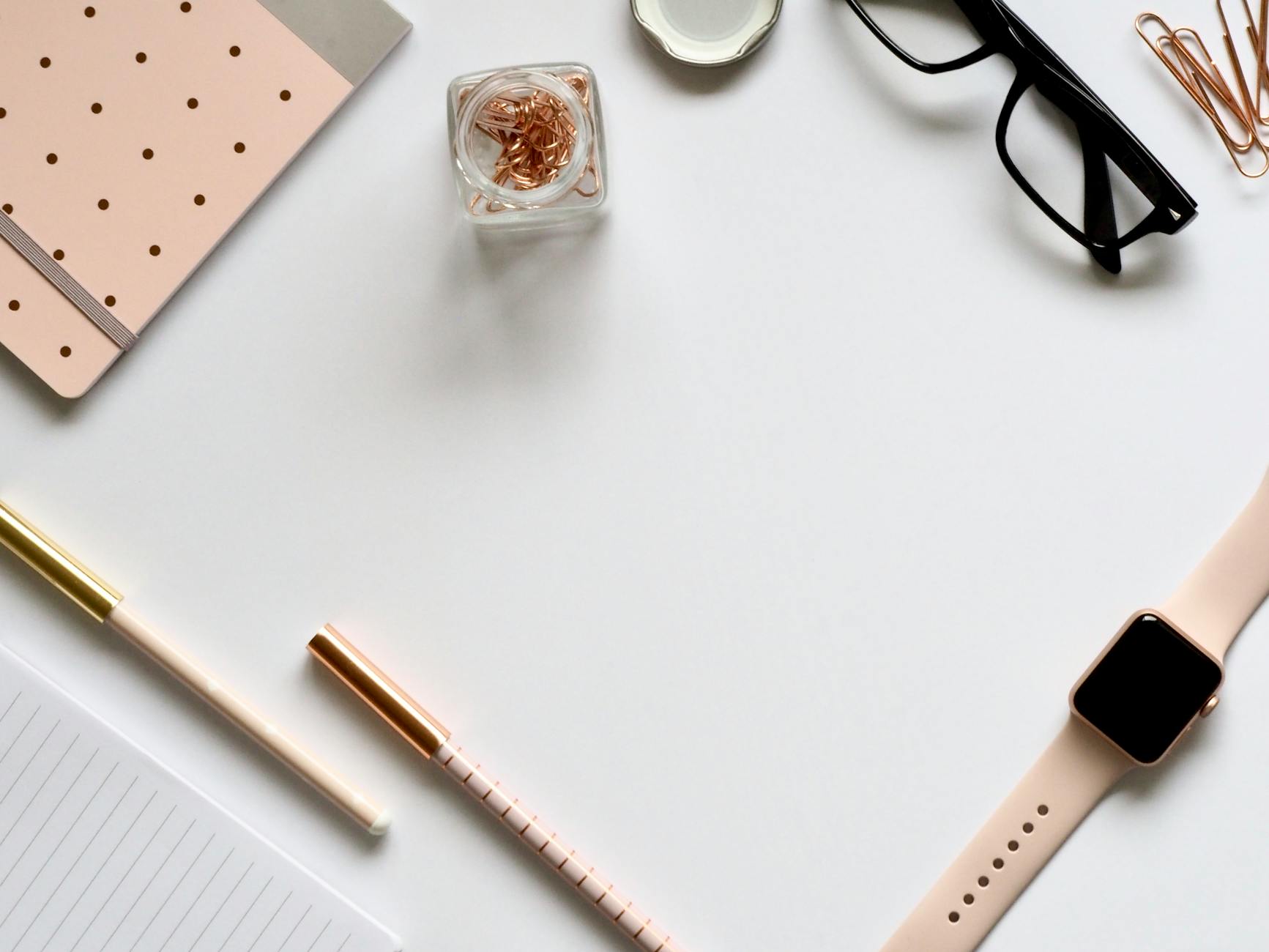 Stylish rose gold themed flatlay featuring office supplies and a smartwatch on a white background.