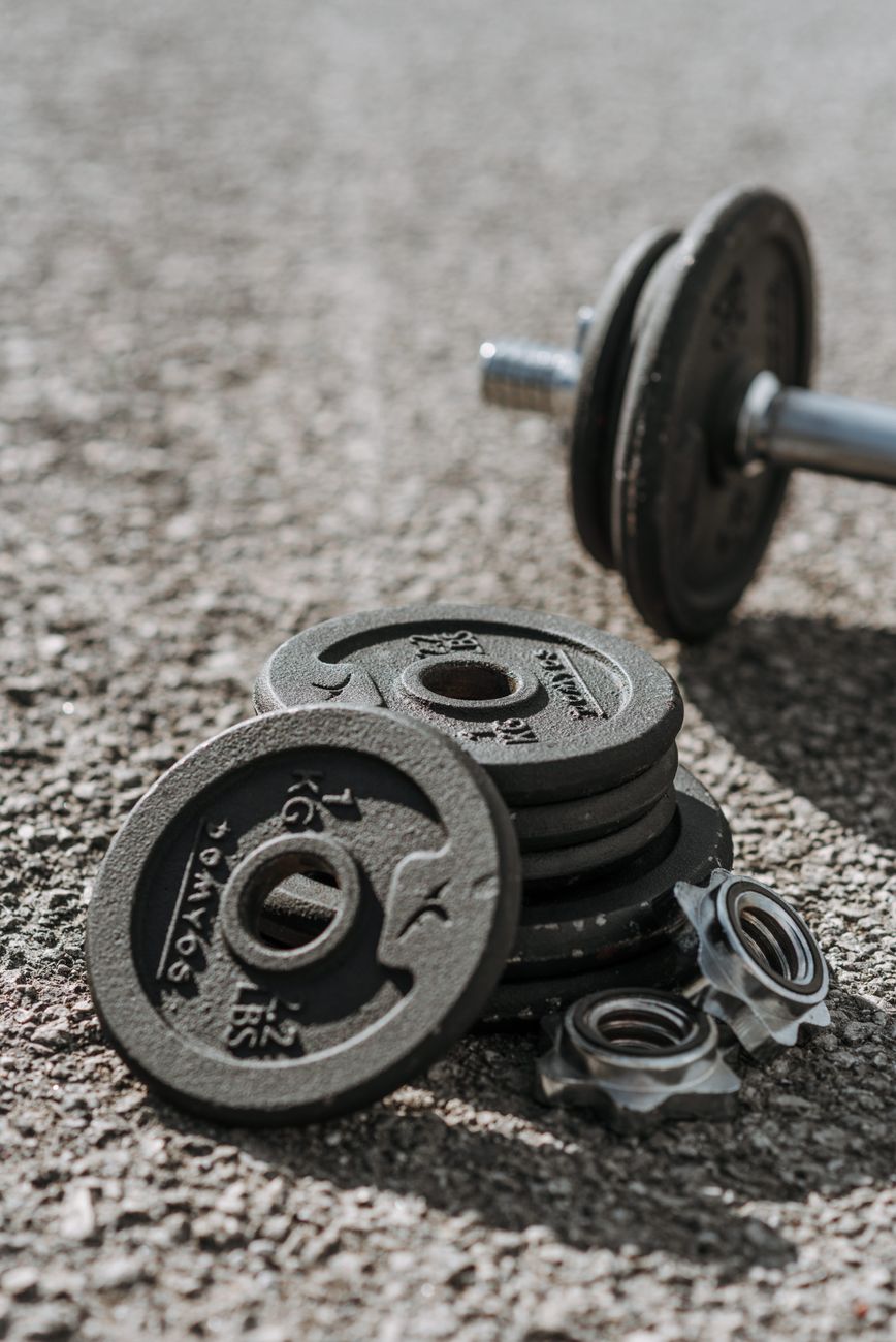 Adjustable dumbbells with weight discs left on asphalt sports ground in bright sunlight