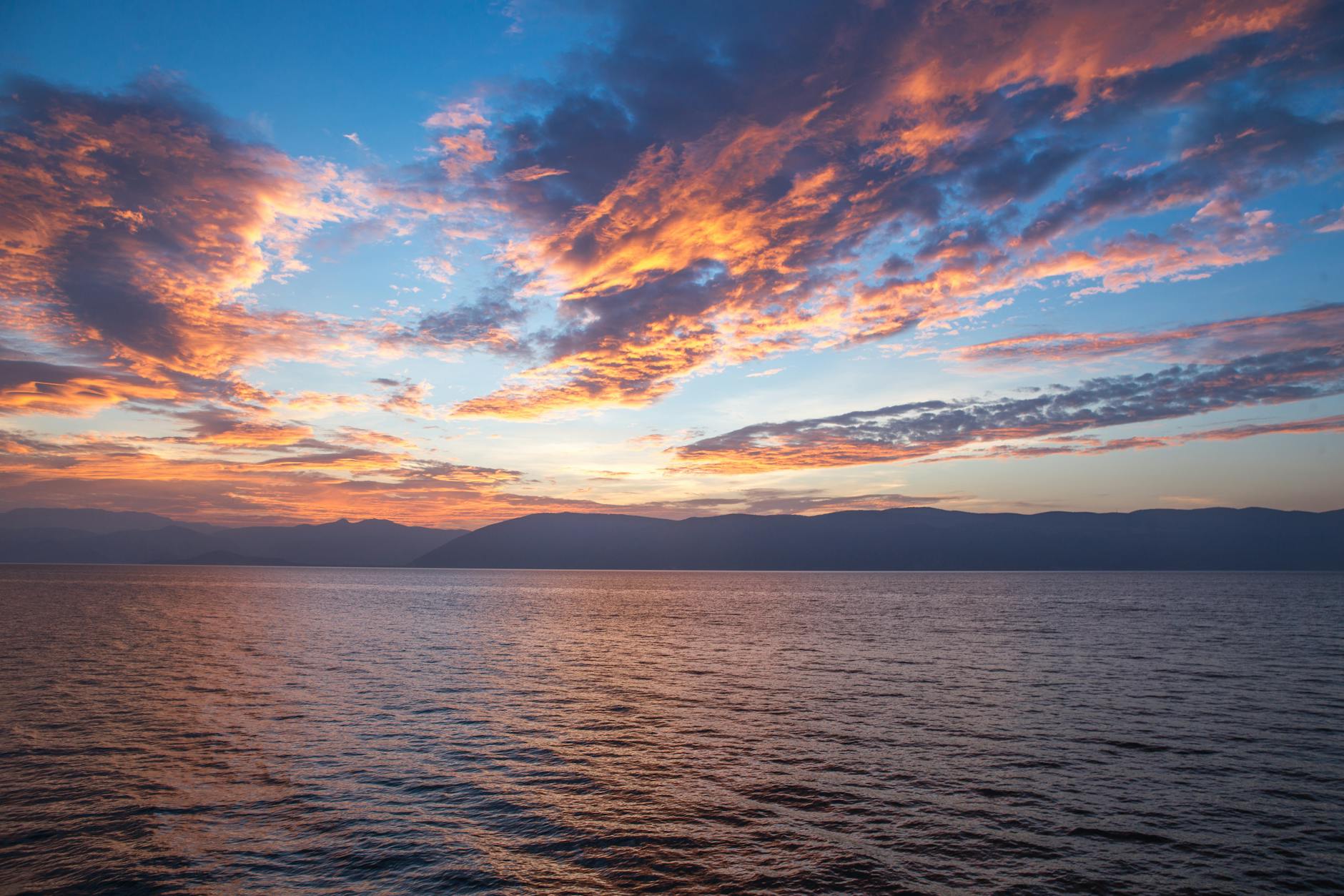 A vibrant sunset with dramatic clouds reflects over the calm ocean, capturing nature's beauty.
