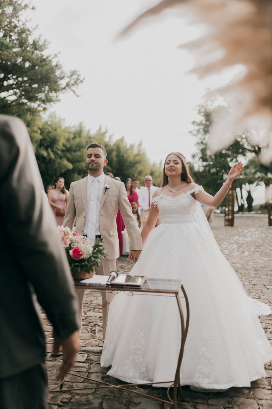 A bride and groom during an outdoor wedding ceremony on a cobblestone path surrounded by nature and guests.