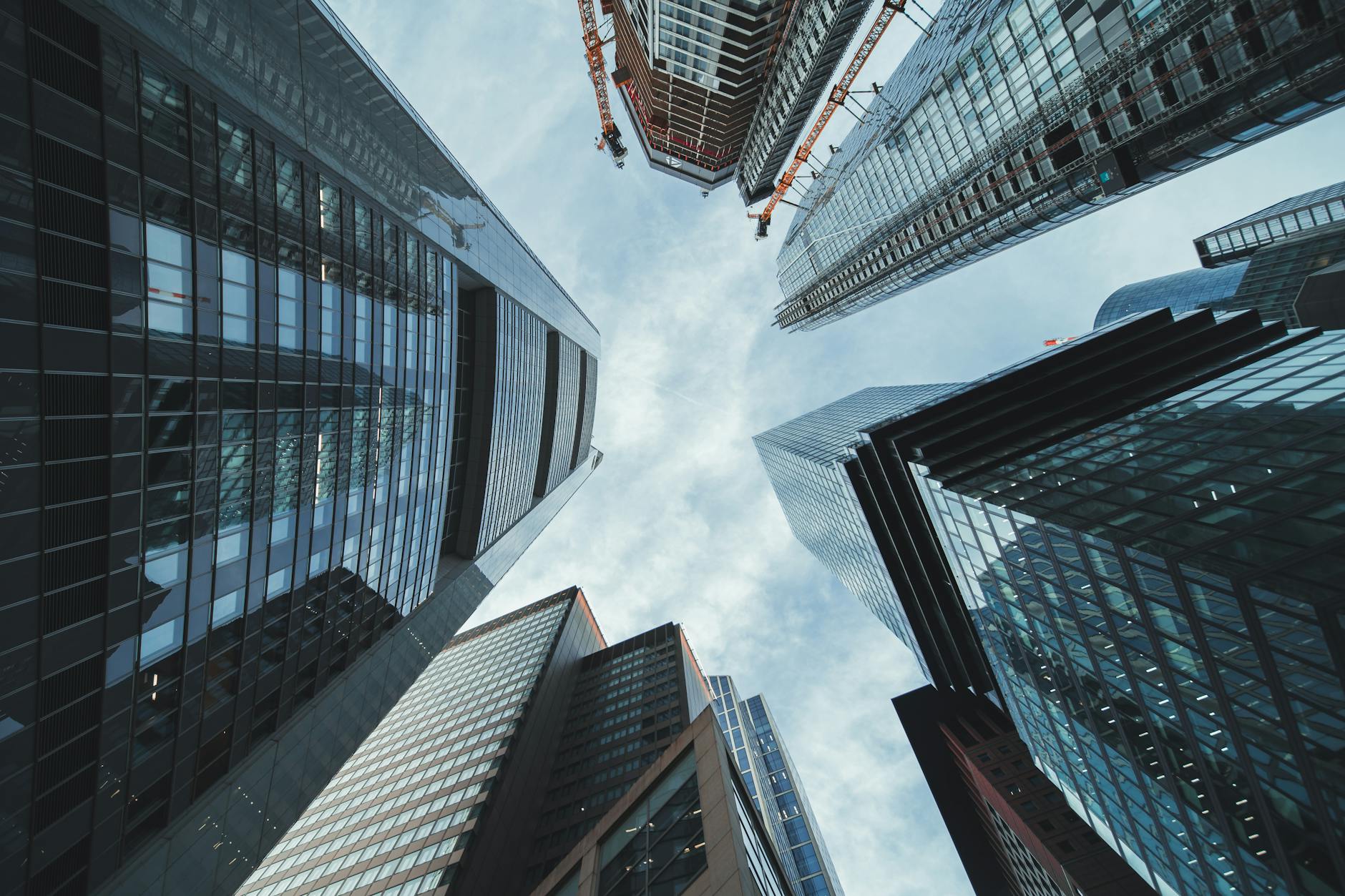 Upward view of towering contemporary skyscrapers against a cloudy blue sky.