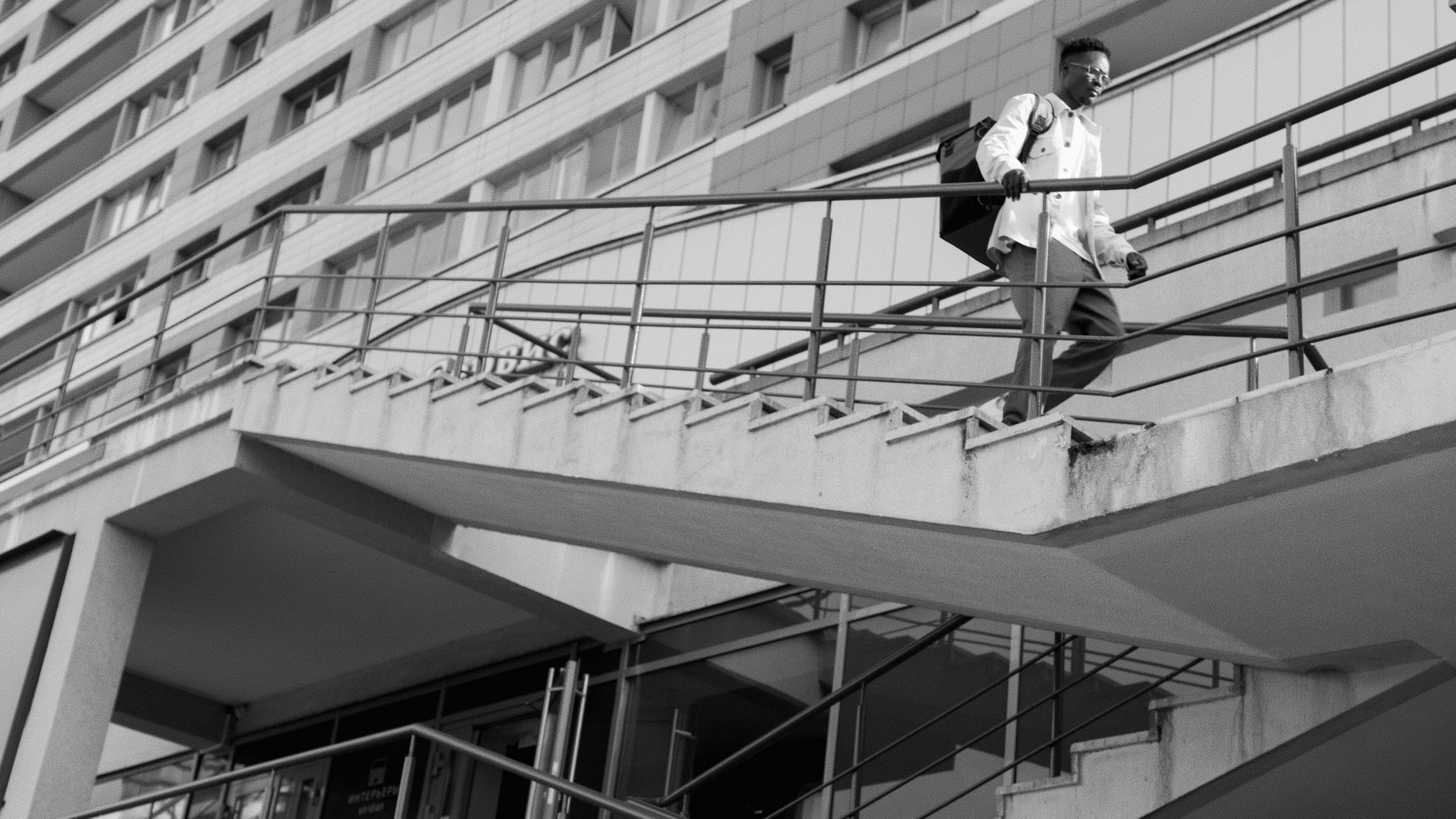 Monochrome image of a person on stairs in front of a modern urban building.