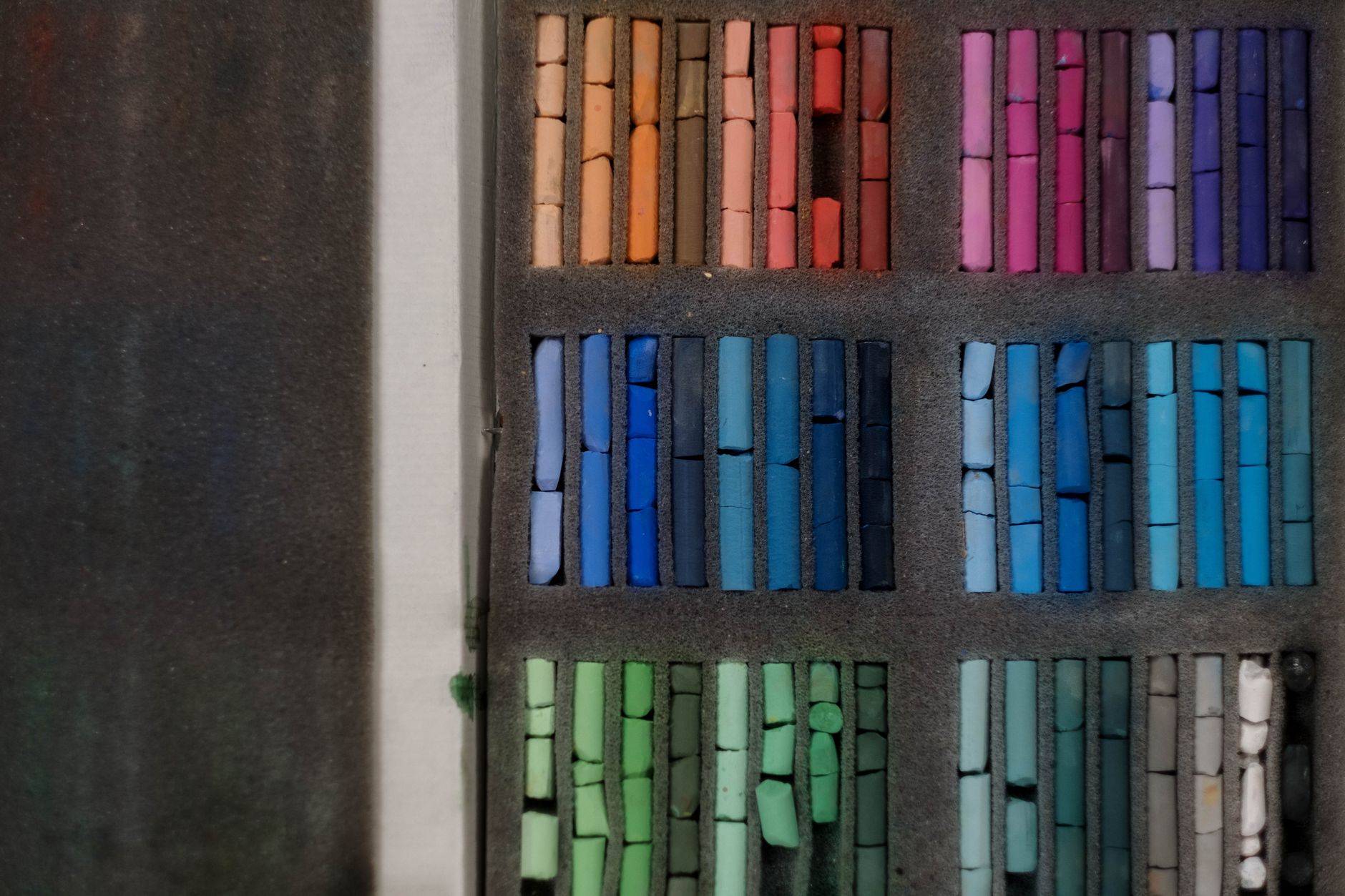 A neatly arranged set of colorful pastels in a display case, showcasing a gradient of vibrant hues.