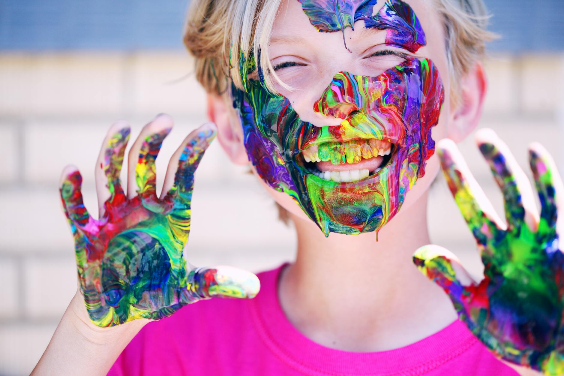 A joyful child with vibrant face paint and hands, expressing happiness and creativity.