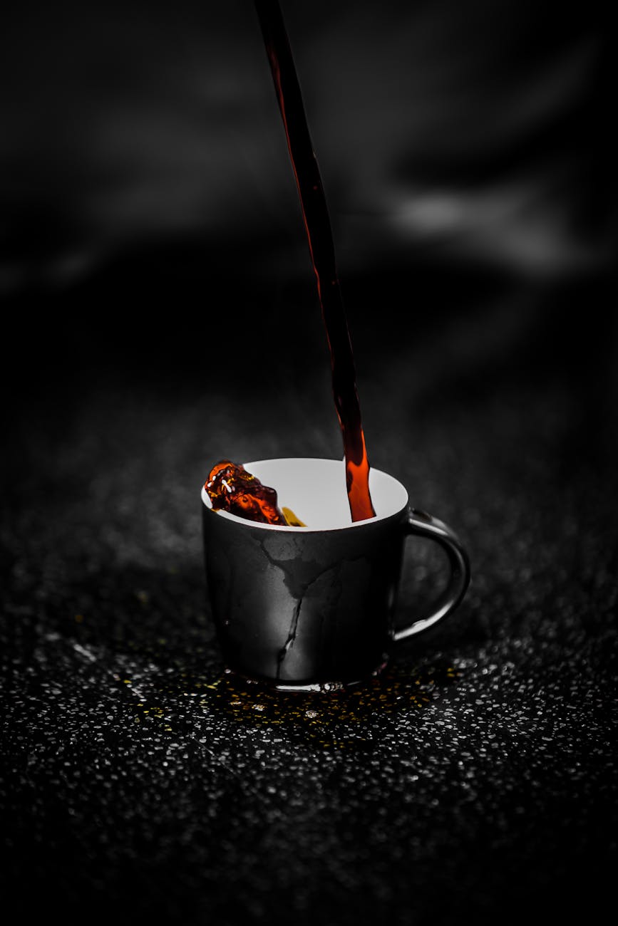 Close-up of steaming dark coffee being poured into a black cup on a dark textured surface. Rich aroma.