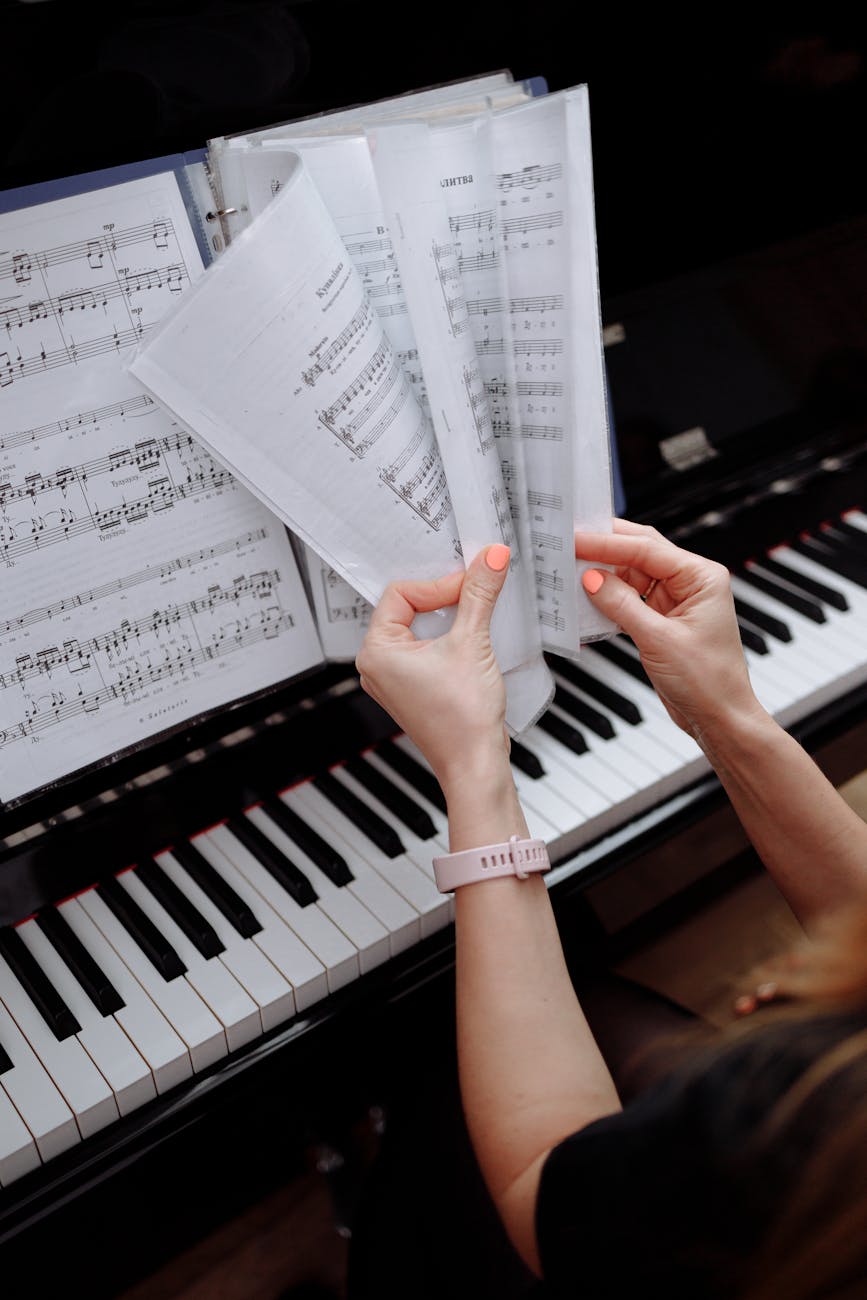 Close-up view of hands flipping through sheet music on a piano, emphasizing musical practice.