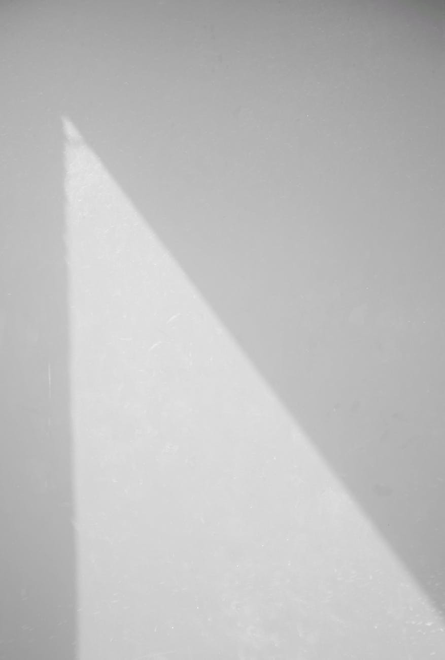 Abstract minimalist photo capturing sunlight casting a triangular shadow on a white wall.