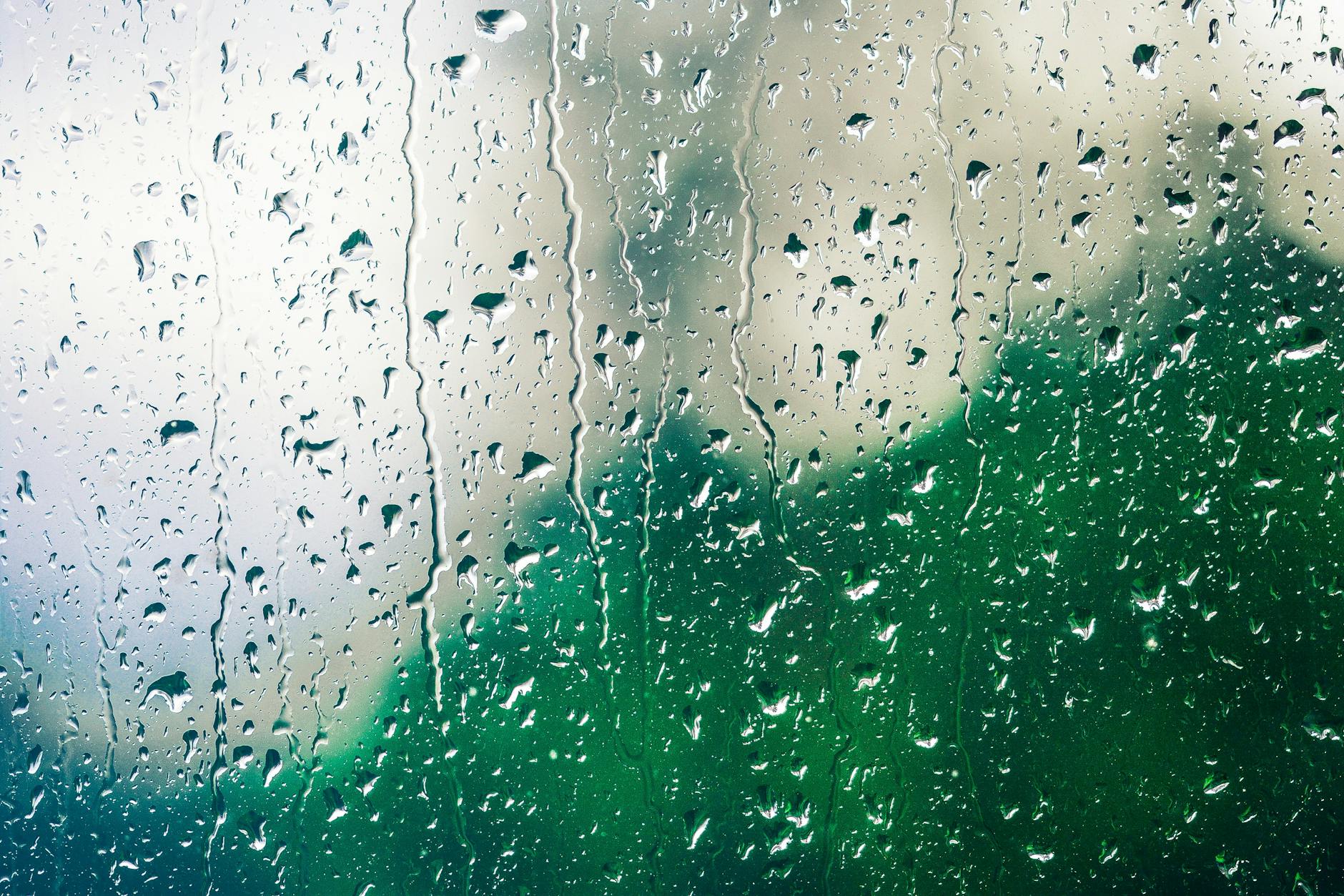 Raindrops on a glass window create a soothing pattern with a blurred green backdrop.