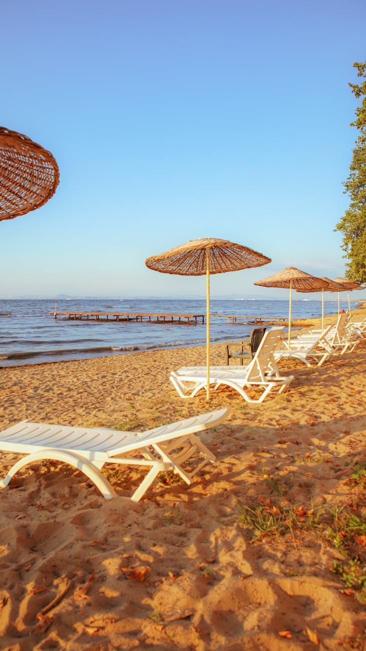 Tranquil sandy beach with sun loungers and umbrellas at sunset, perfect for relaxation.