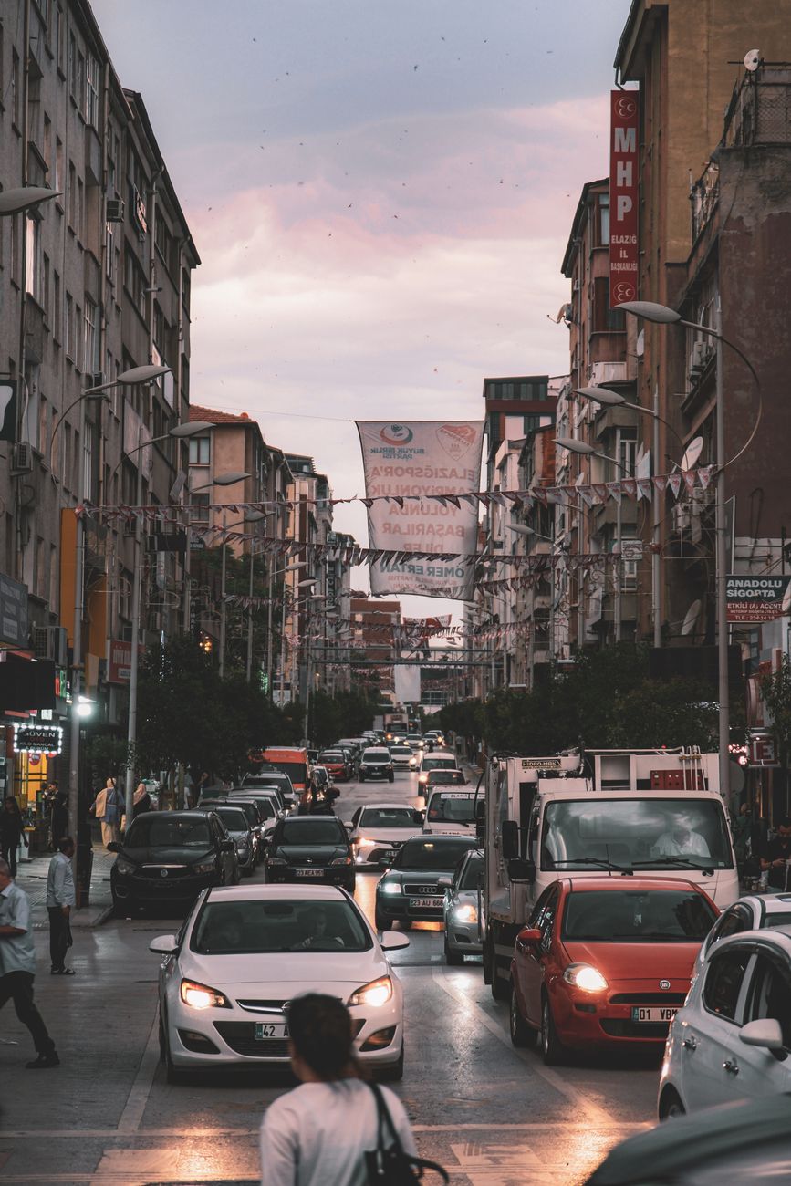 Traffic jams a busy city street at dusk, surrounded by tall buildings and vibrant urban life.