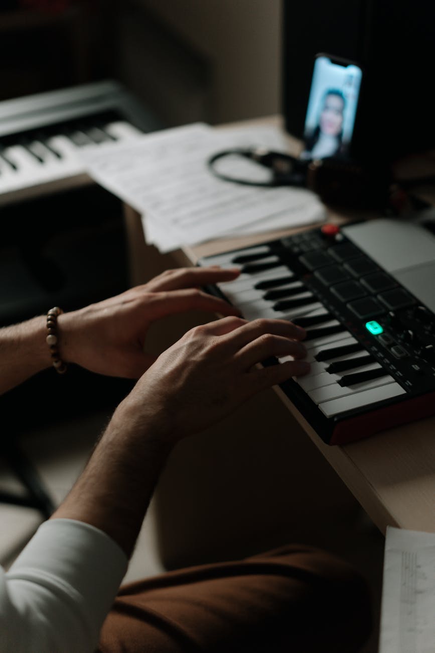 A close-up of hands playing a synthesizer indoors, capturing the creative process of composing music.