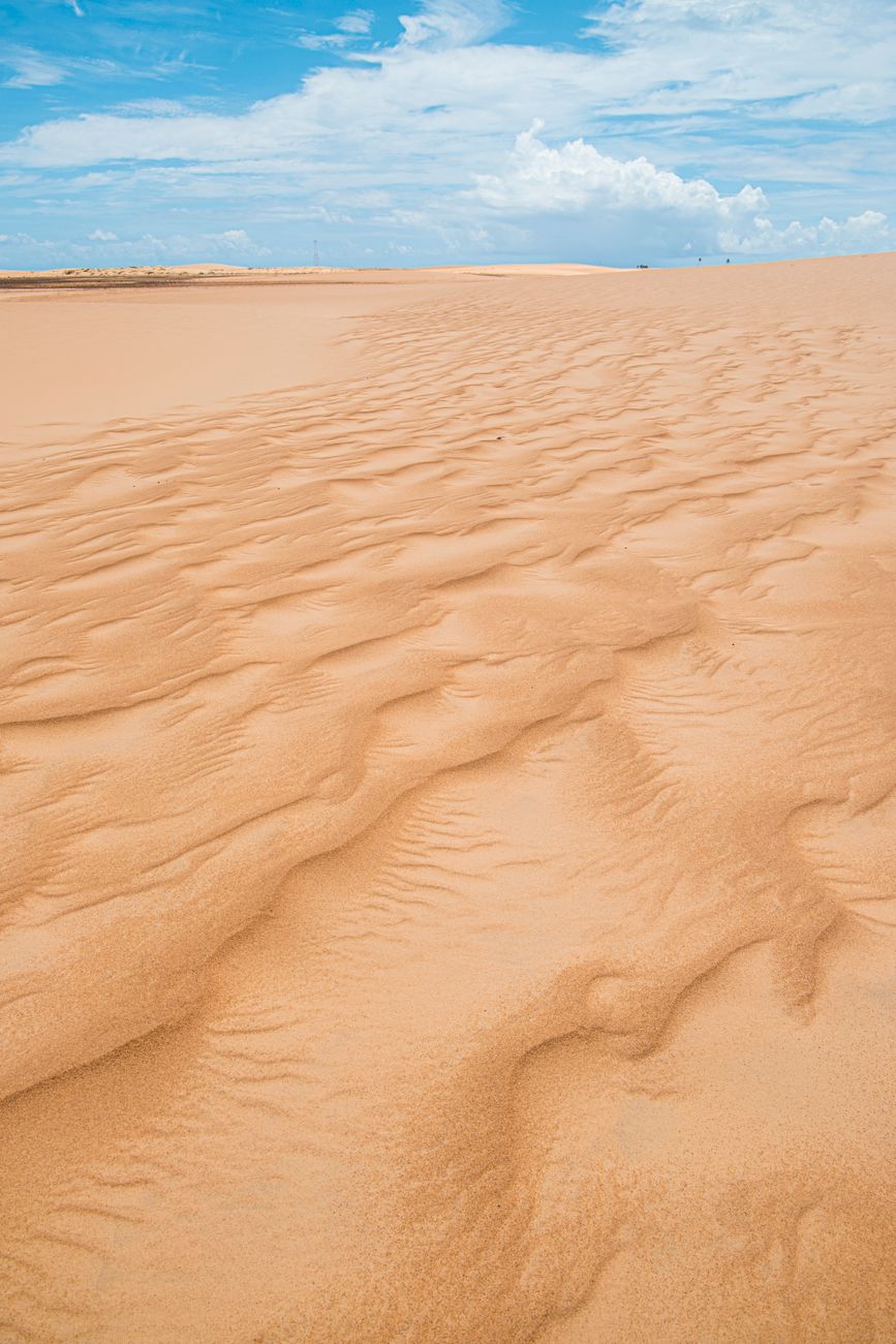 Expansive sandy dunes under a bright blue sky in Piaçabuçu, Brazil.