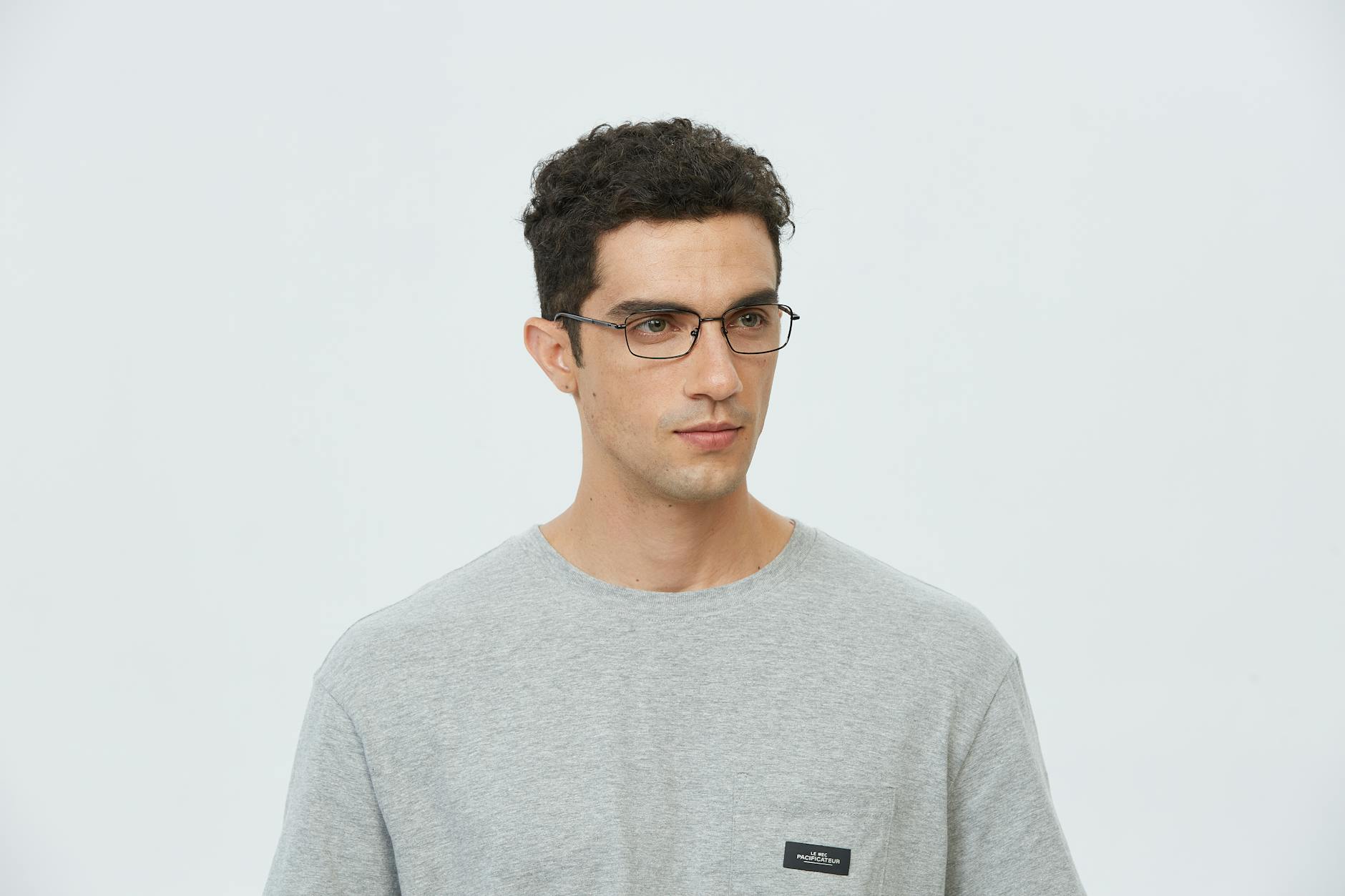 Portrait of a young man wearing glasses and a gray T-shirt in a studio setting.