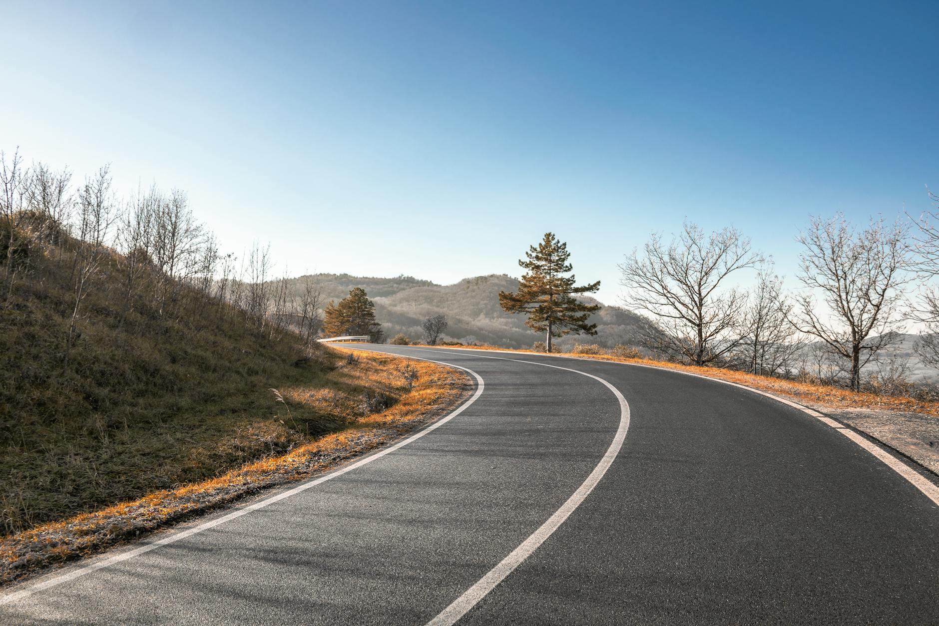 Scenic view of a winding road amidst autumn landscape with clear blue skies.