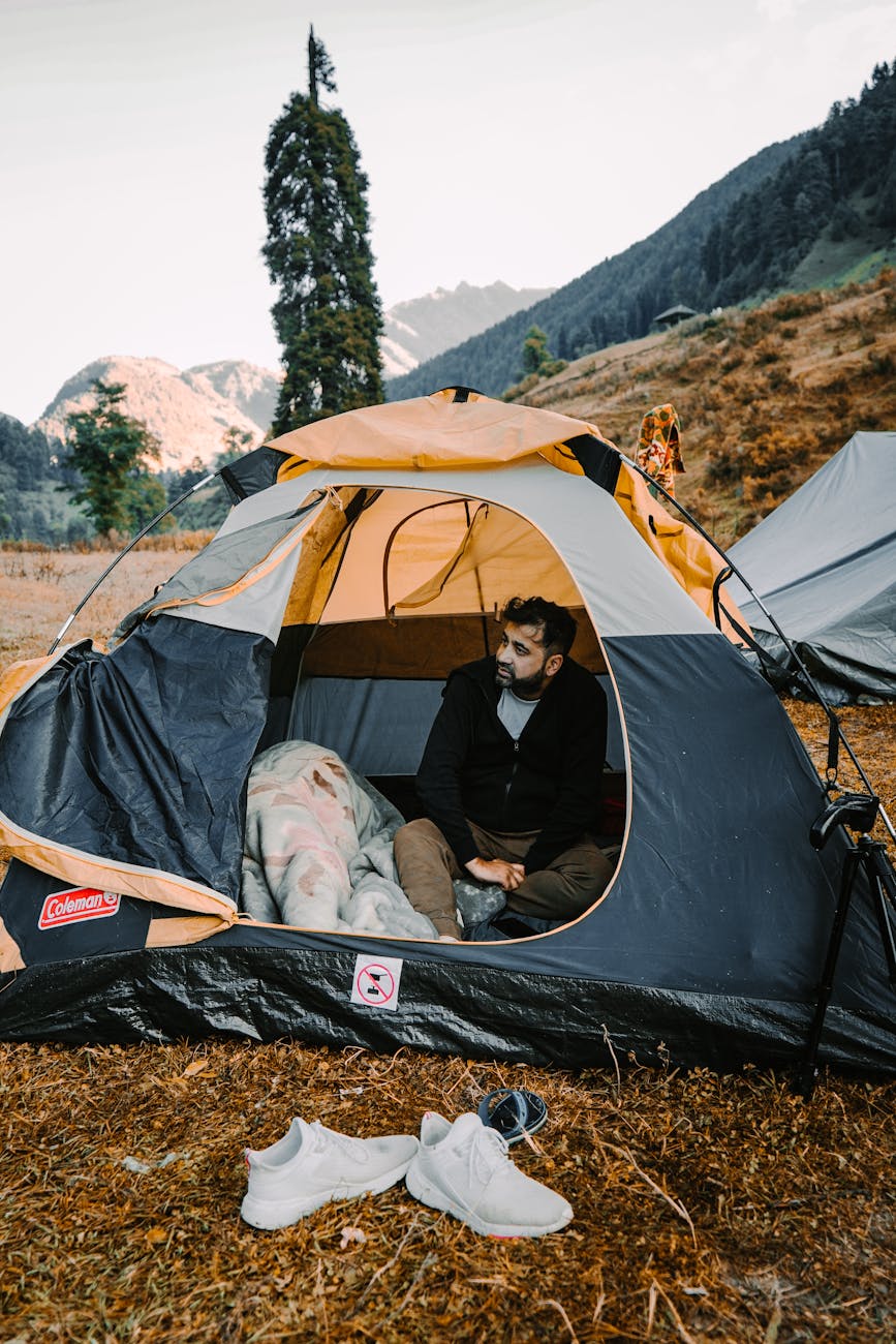 A man sitting inside a tent in a mountainous outdoor setting, enjoying nature.